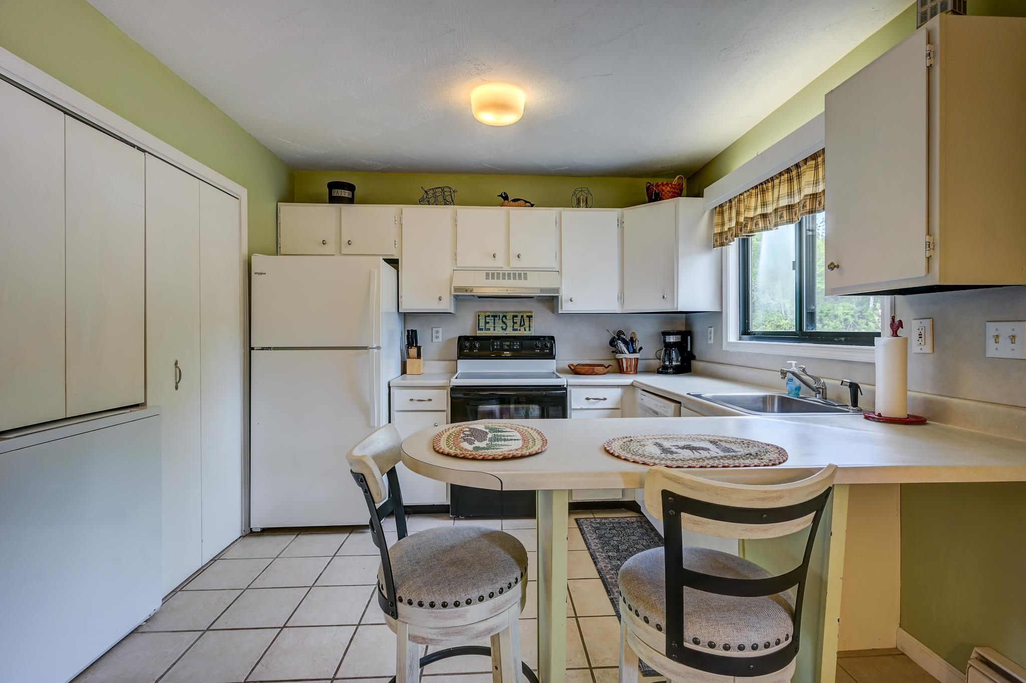 Kitchen with white cabinets, a breakfast counter, and a large window above the sink.