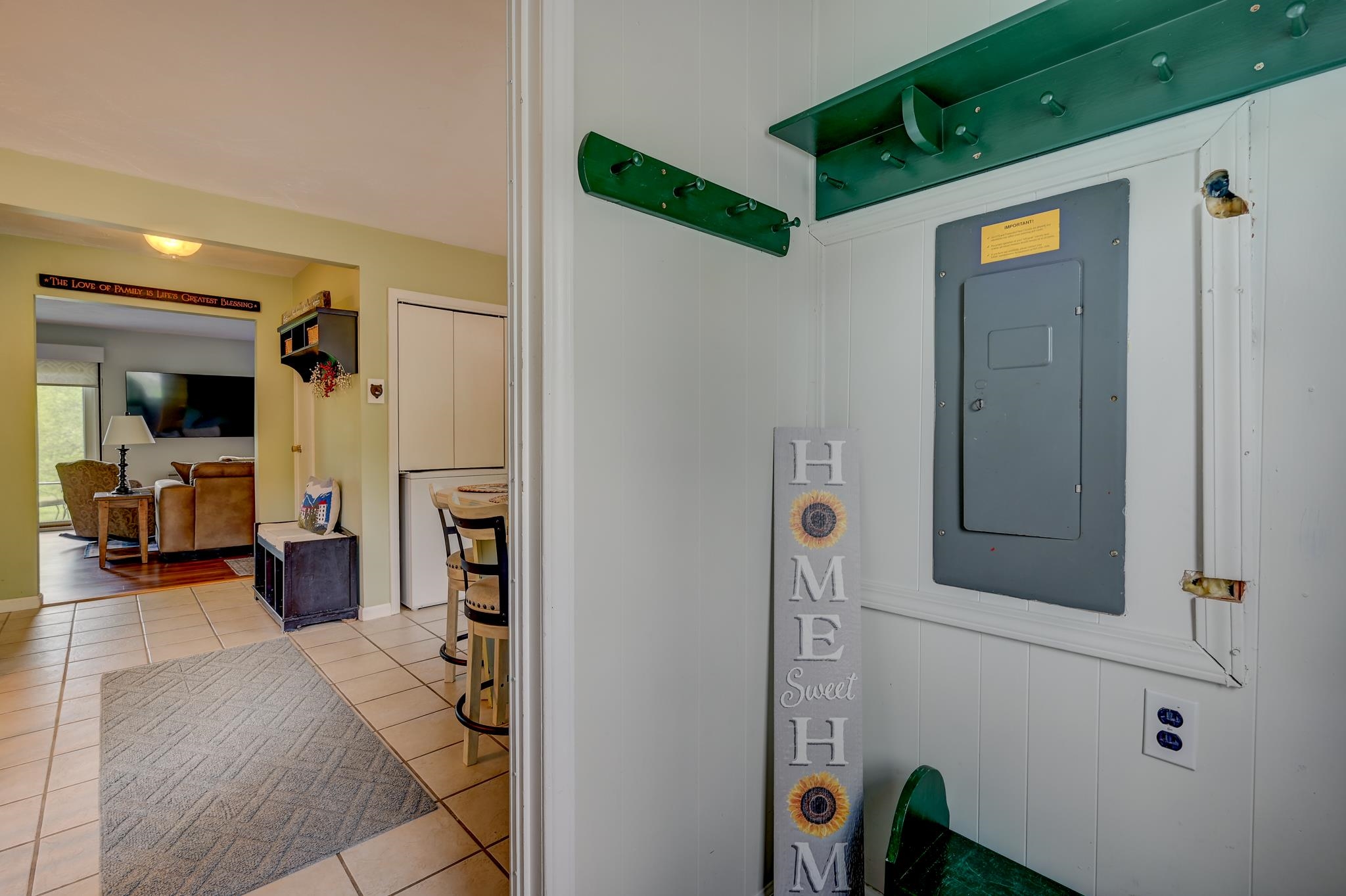 Tiled home entry with green coat racks, a HOME sign, and a view into the living room.