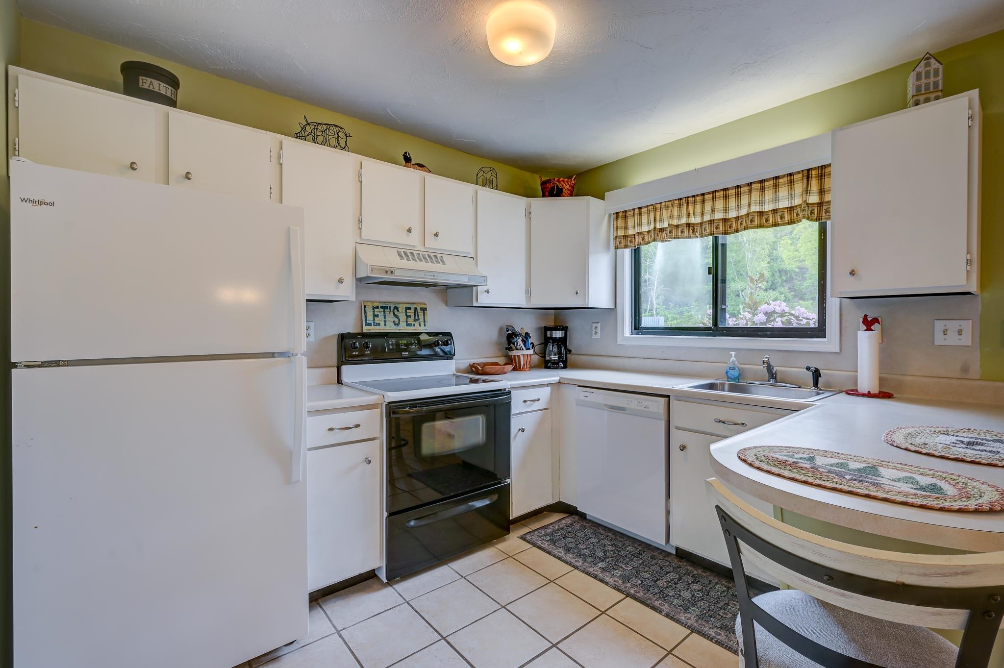 Kitchen with white cabinets and appliances, a window overlooking greenery, and a rounded breakfast counter.