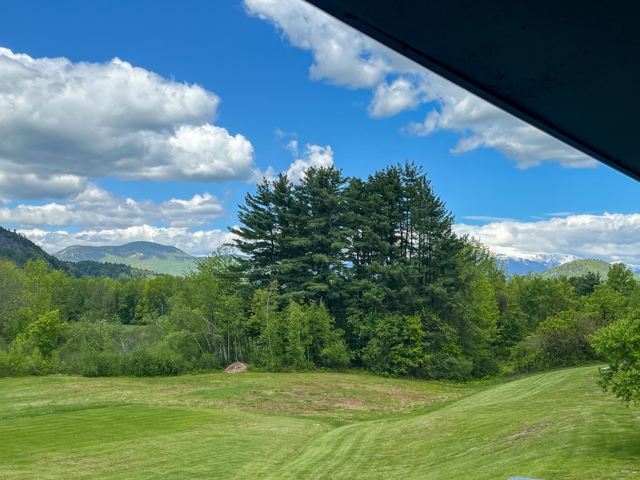 Green lawn and evergreen trees frame a distant mountain range beneath a cloud-filled sky.