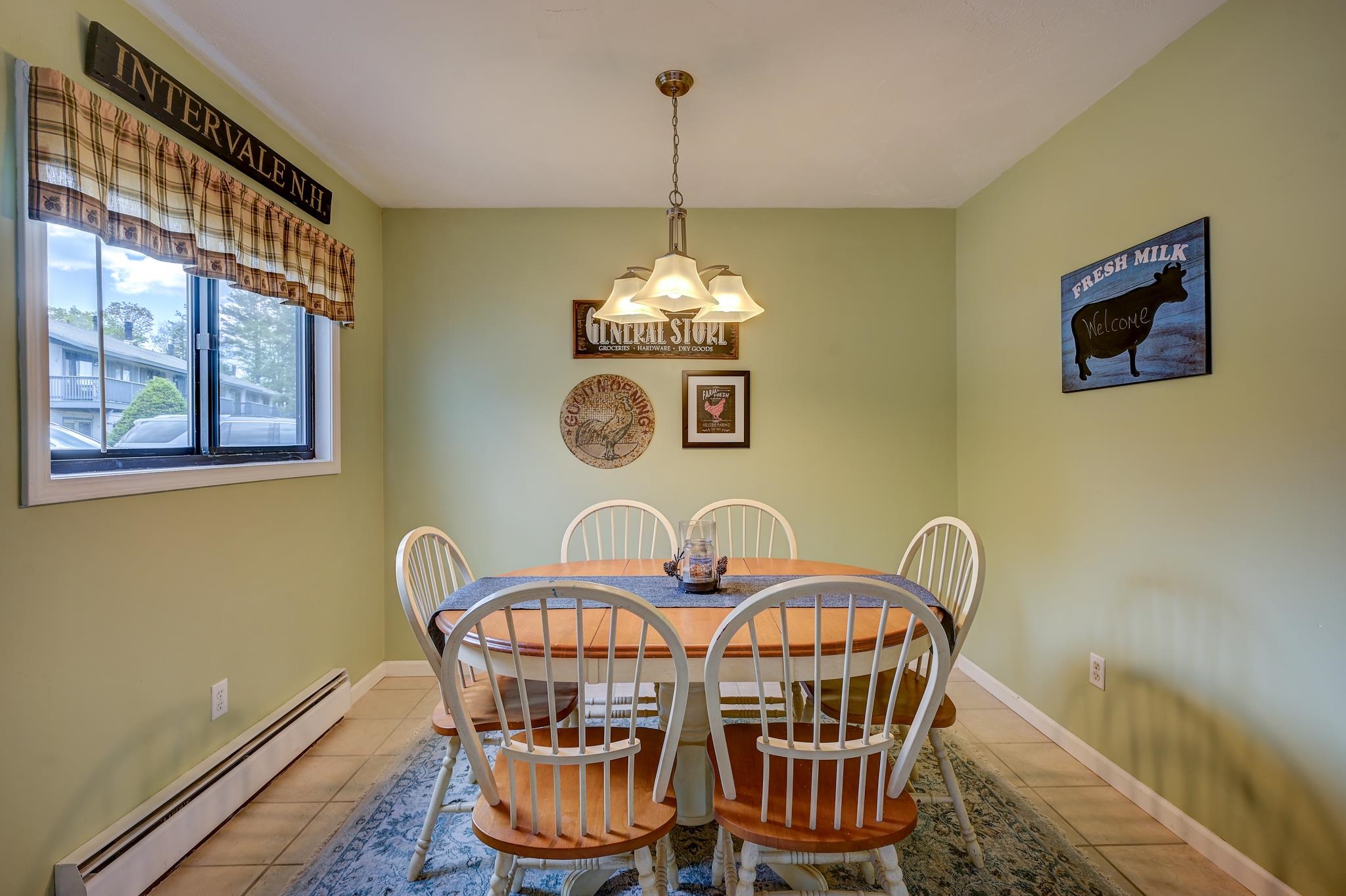 Dining room with a round wooden table, white chairs, plaid curtains, and rustic wall signs.