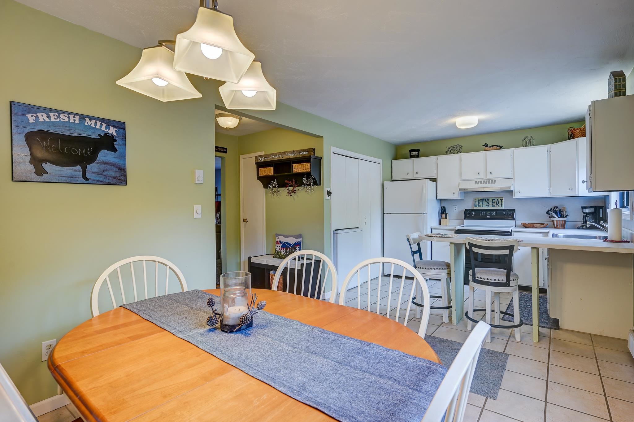 Kitchen and dining area with white cabinetry, tiled floors, and a wooden table with white chairs.