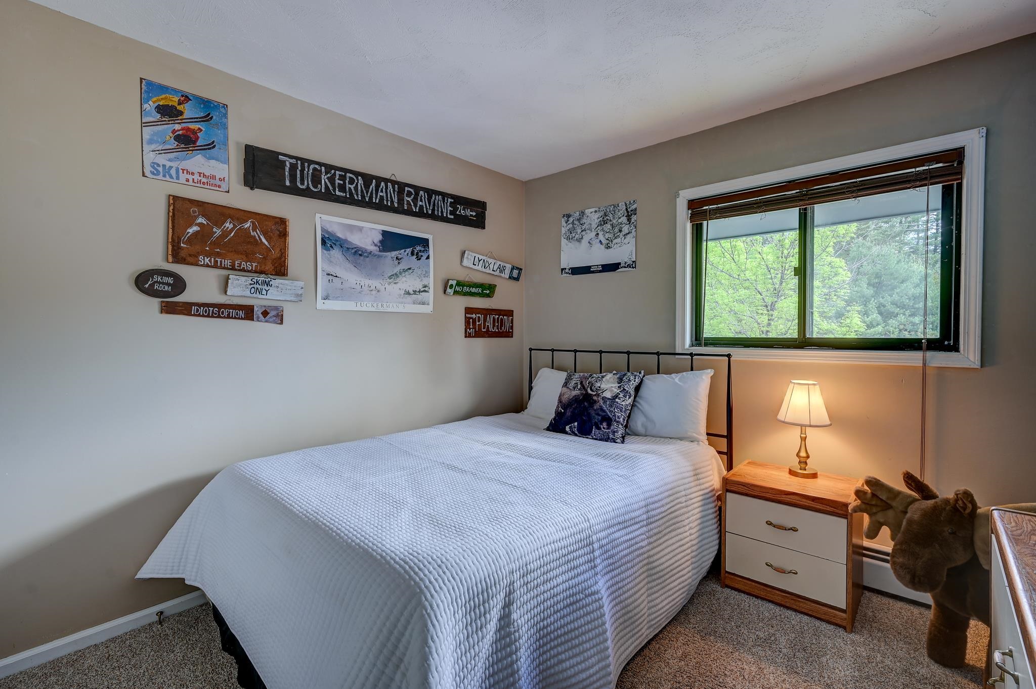 Bedroom with a white quilted bed, ski-themed wall signs, and a window overlooking leafy trees.
