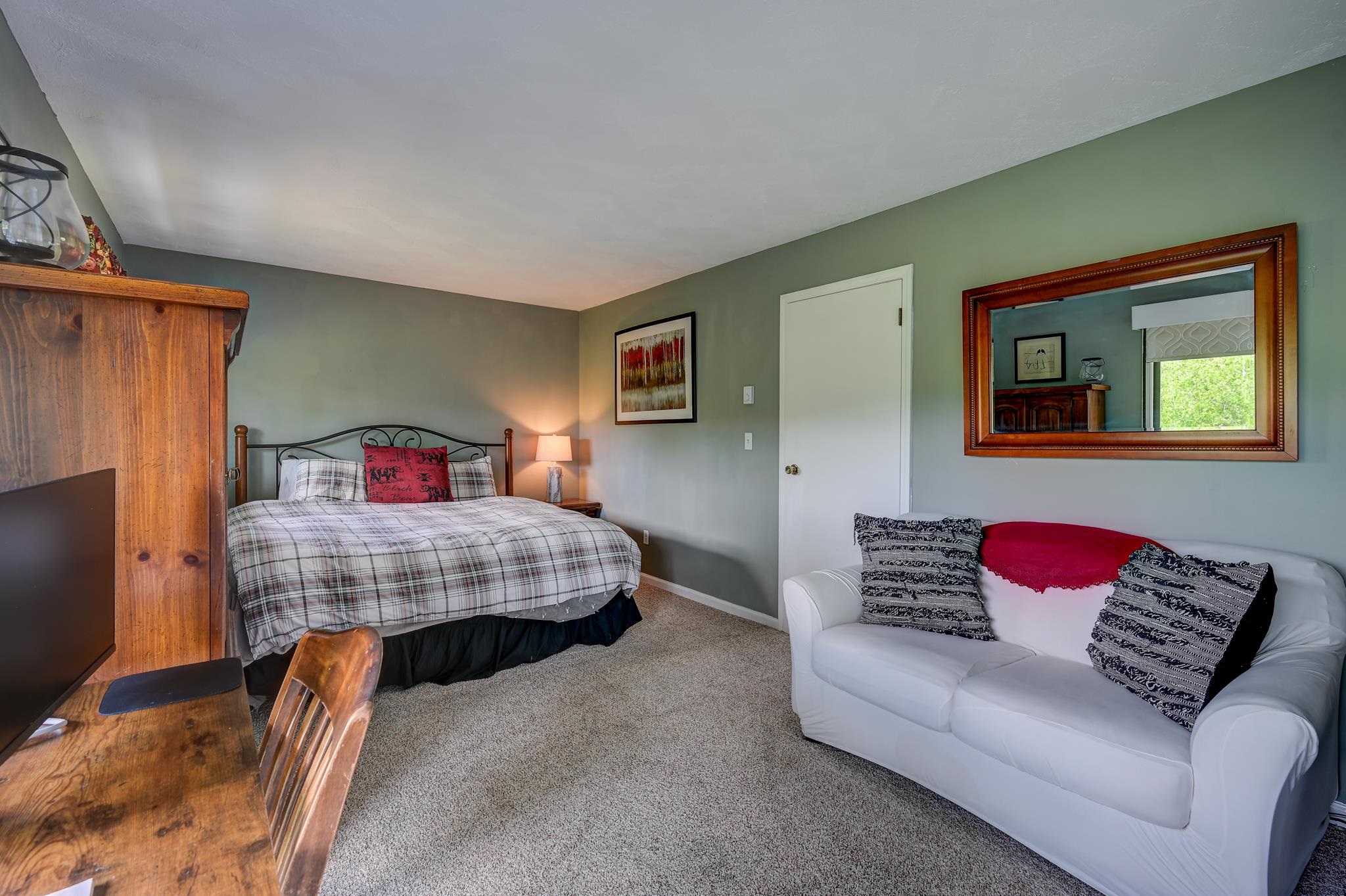 Bedroom with a plaid-covered bed, white sofa, and rustic wooden furniture.