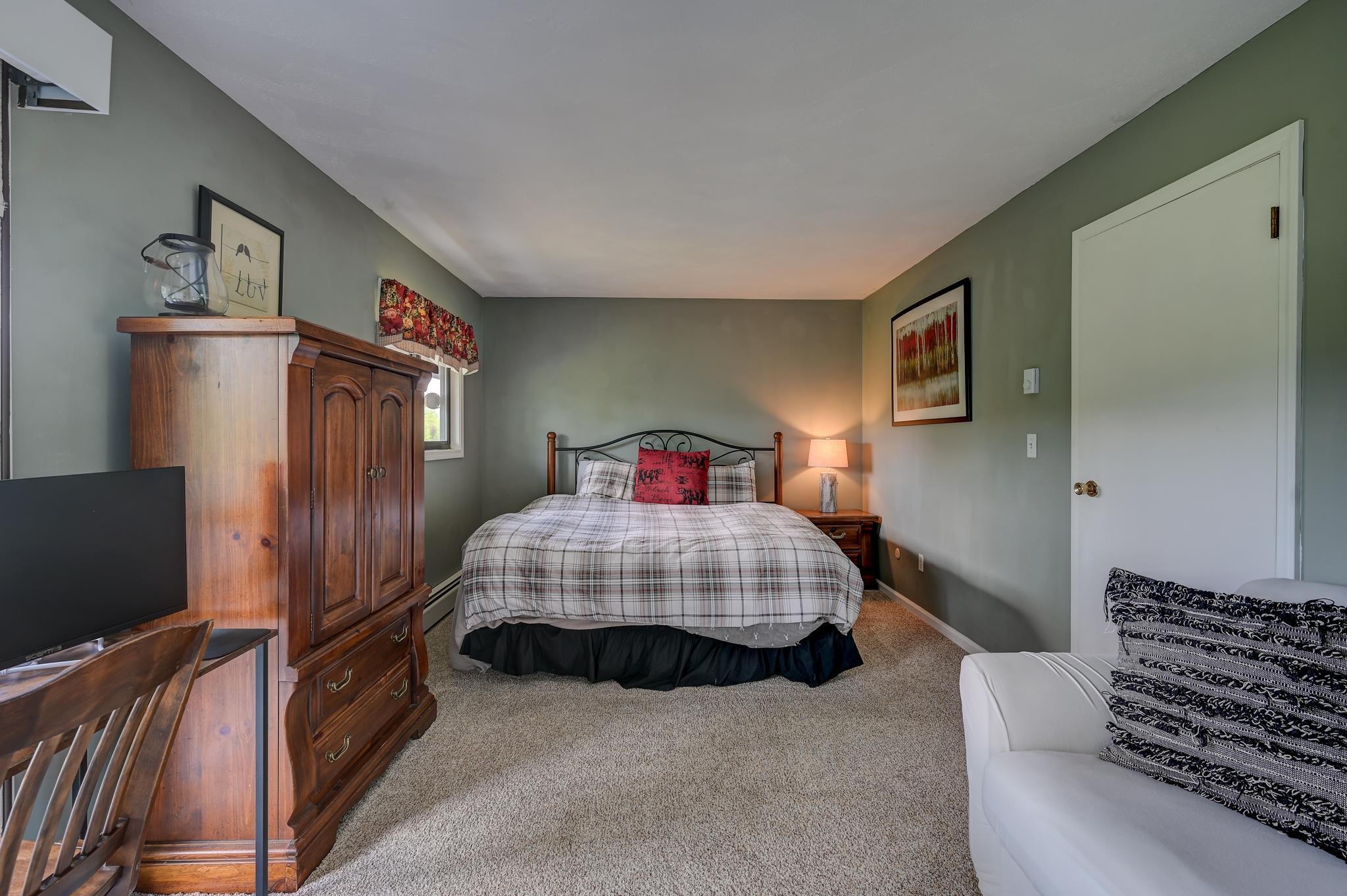 Furnished bedroom with a plaid-covered bed, wooden armoire, and white sofa.