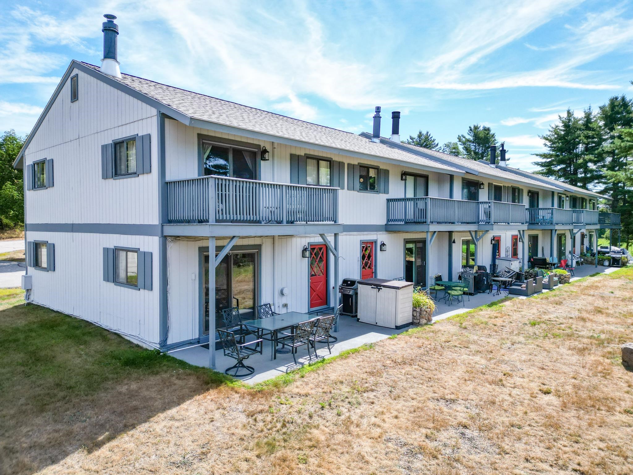 White two-story condominium row with gray balconies, red doors, and furnished patios.