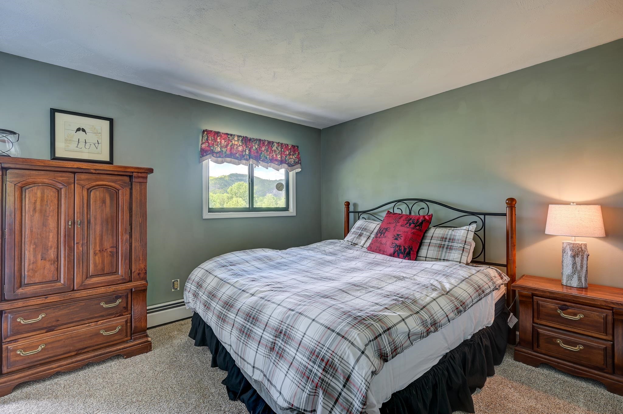 Furnished bedroom with plaid bedding, a wooden armoire, and a mountain view through the window.