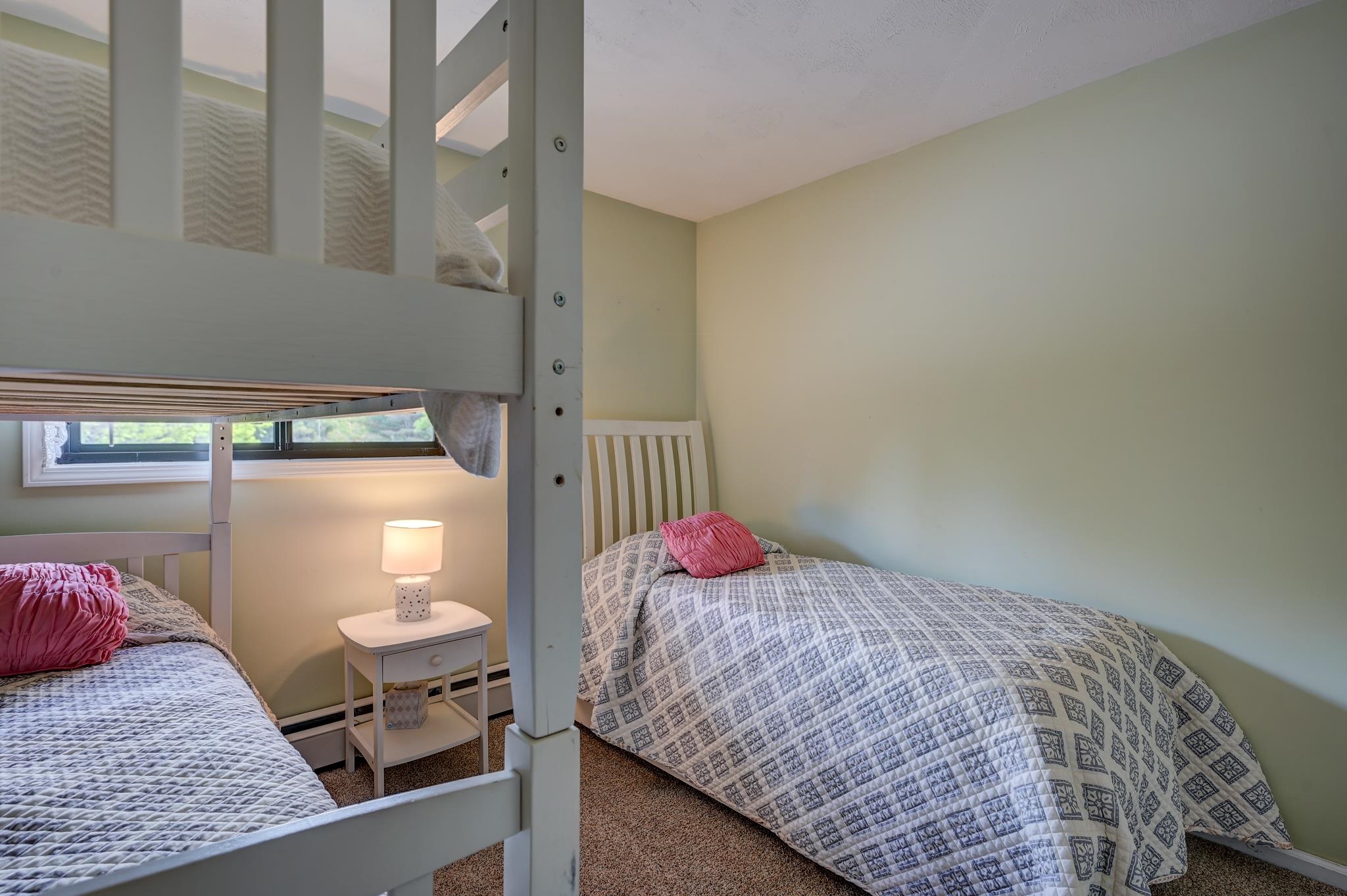Bedroom with white bunk beds, patterned quilts, pink pillows, and a bedside lamp.