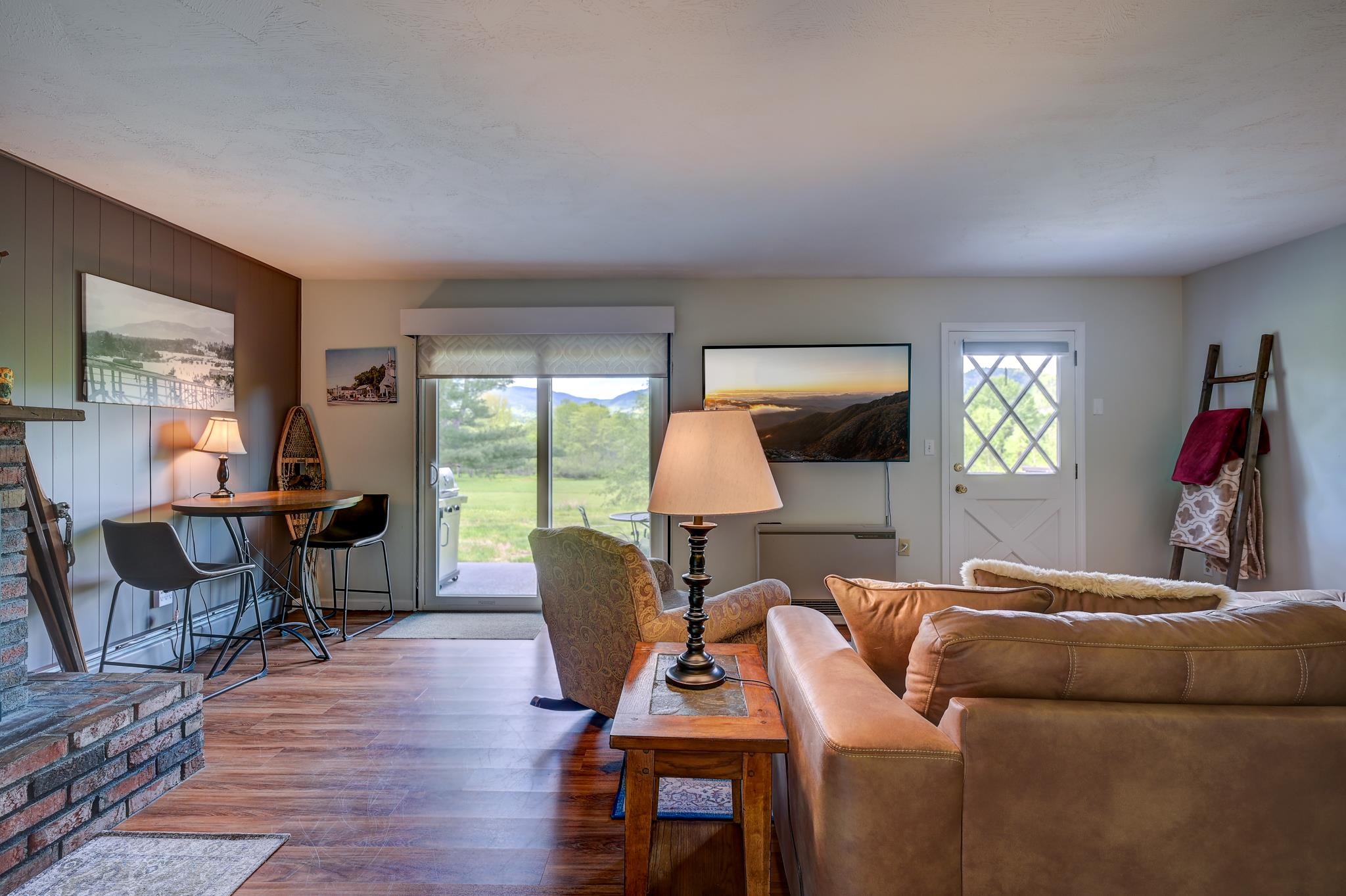 Living room with a brick fireplace, leather sofa, and sliding glass door overlooking greenery and mountains.