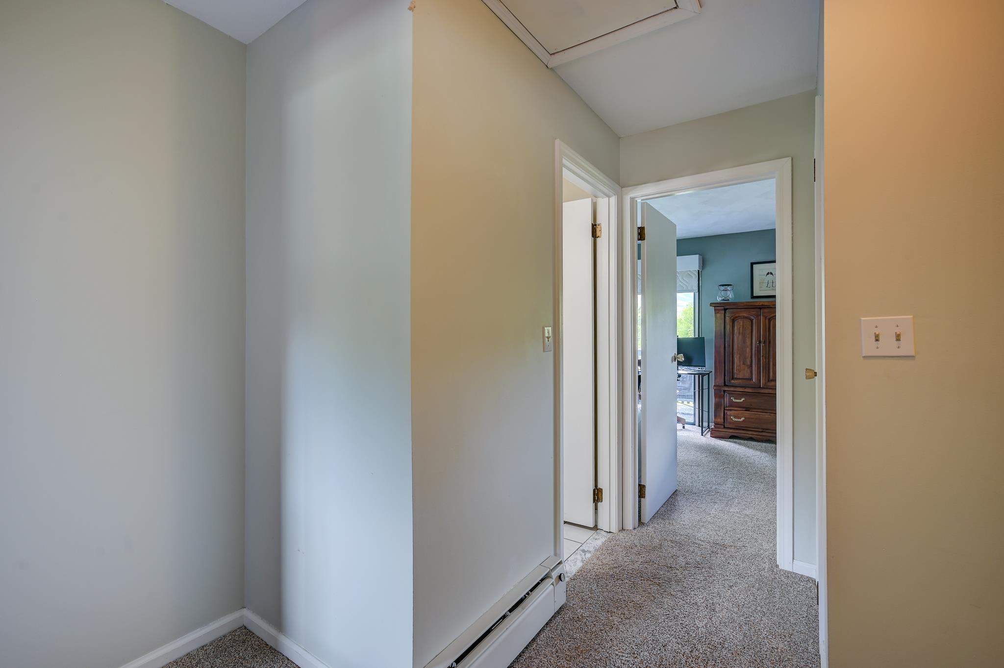 Carpeted hallway with open doorways leading to a bedroom with a wooden armoire.