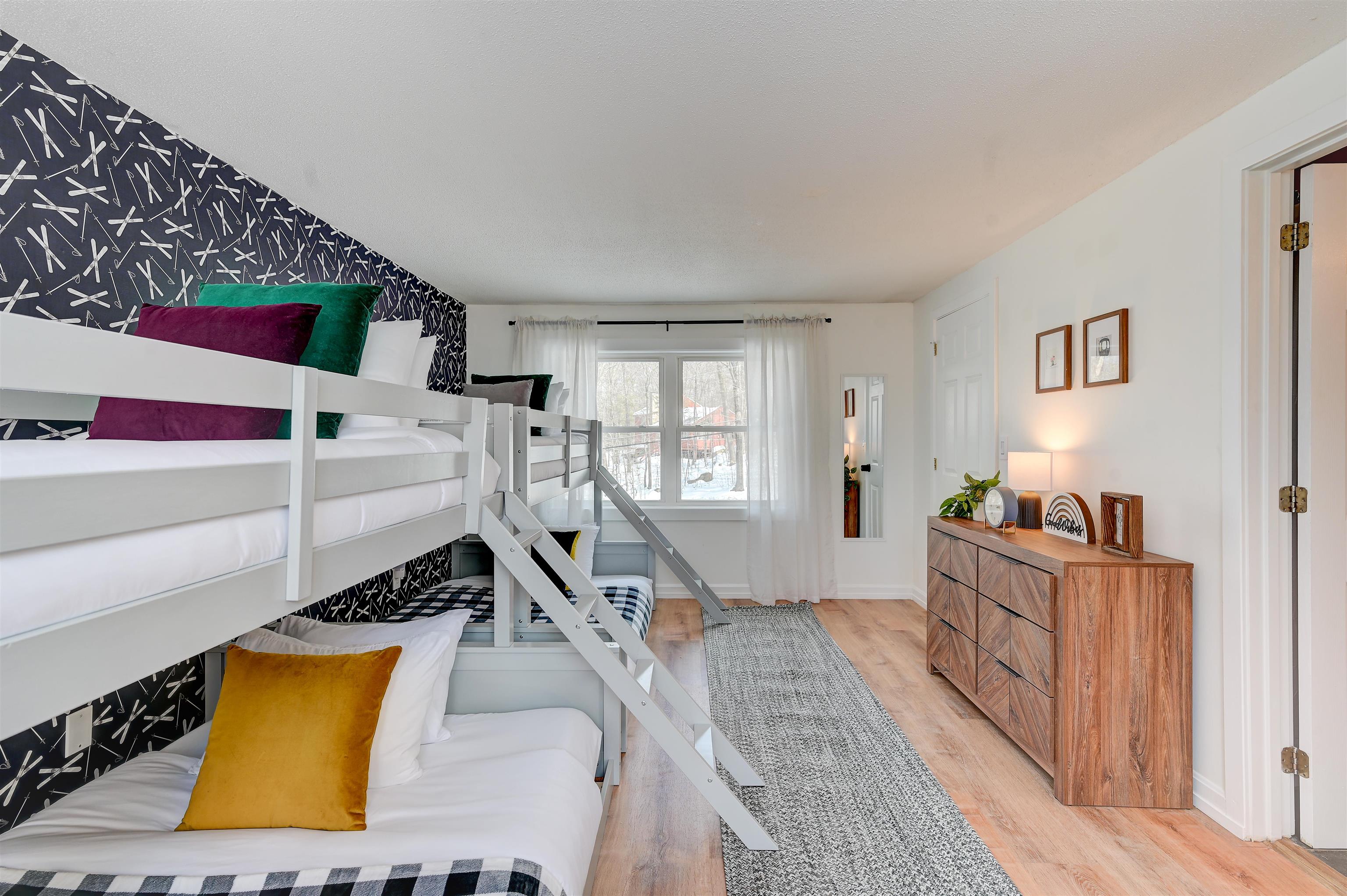 Bedroom with white bunk beds, colorful pillows, patterned accent wall, and a dresser.