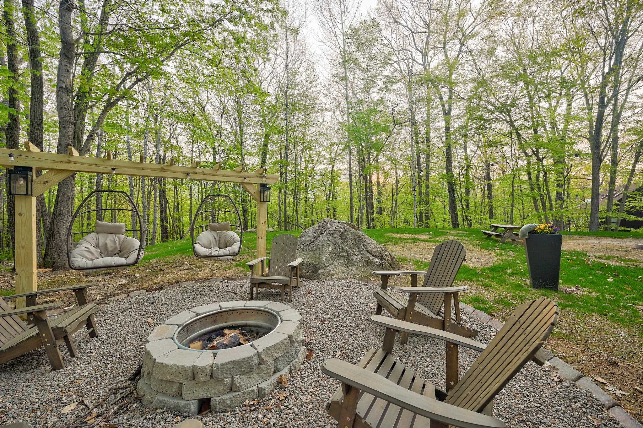 Wooded patio with a stone fire pit, Adirondack chairs, and hanging swing chairs beneath a pergola.