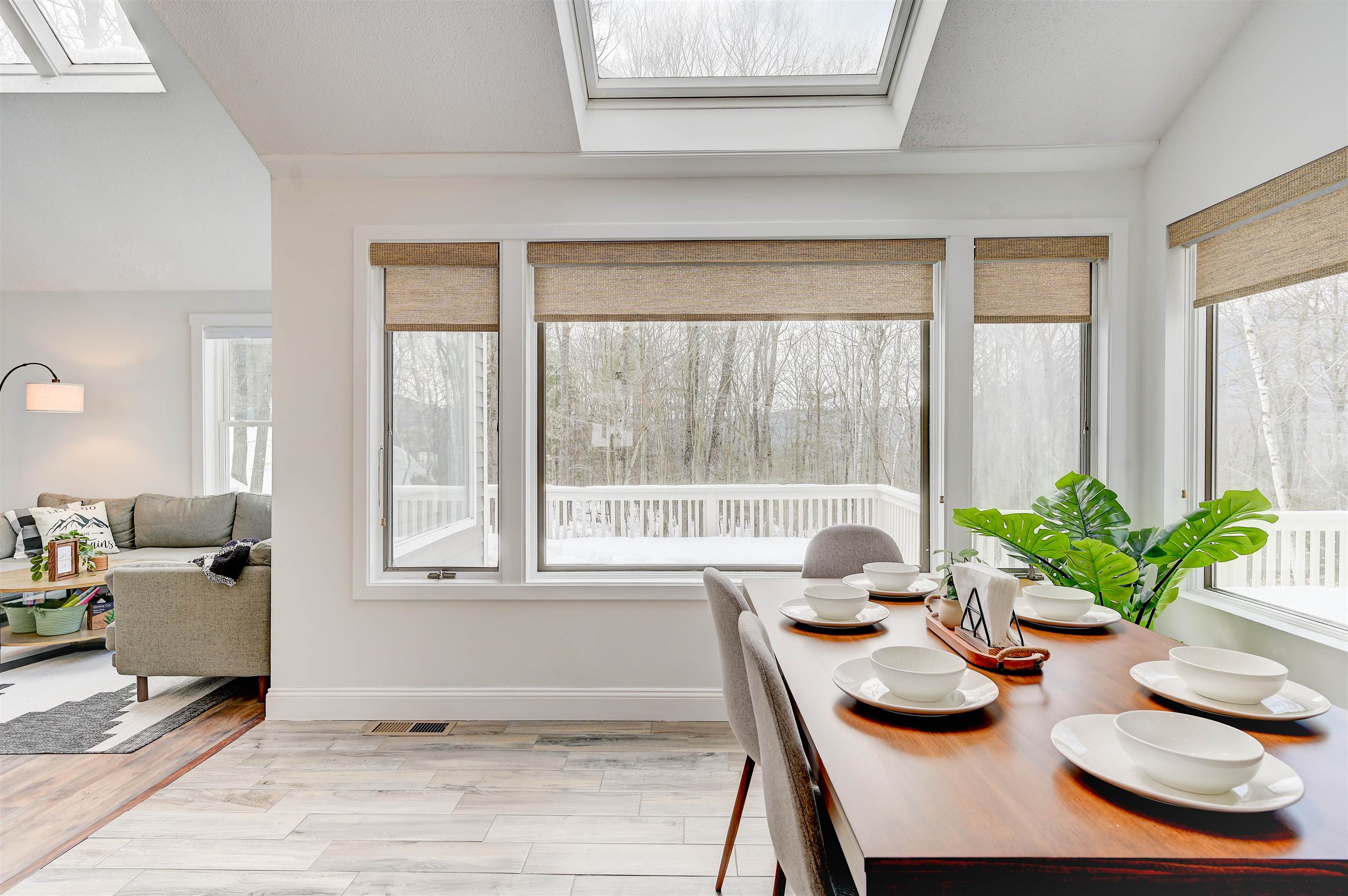 Dining area with a set table, large windows overlooking winter woods, and skylights.