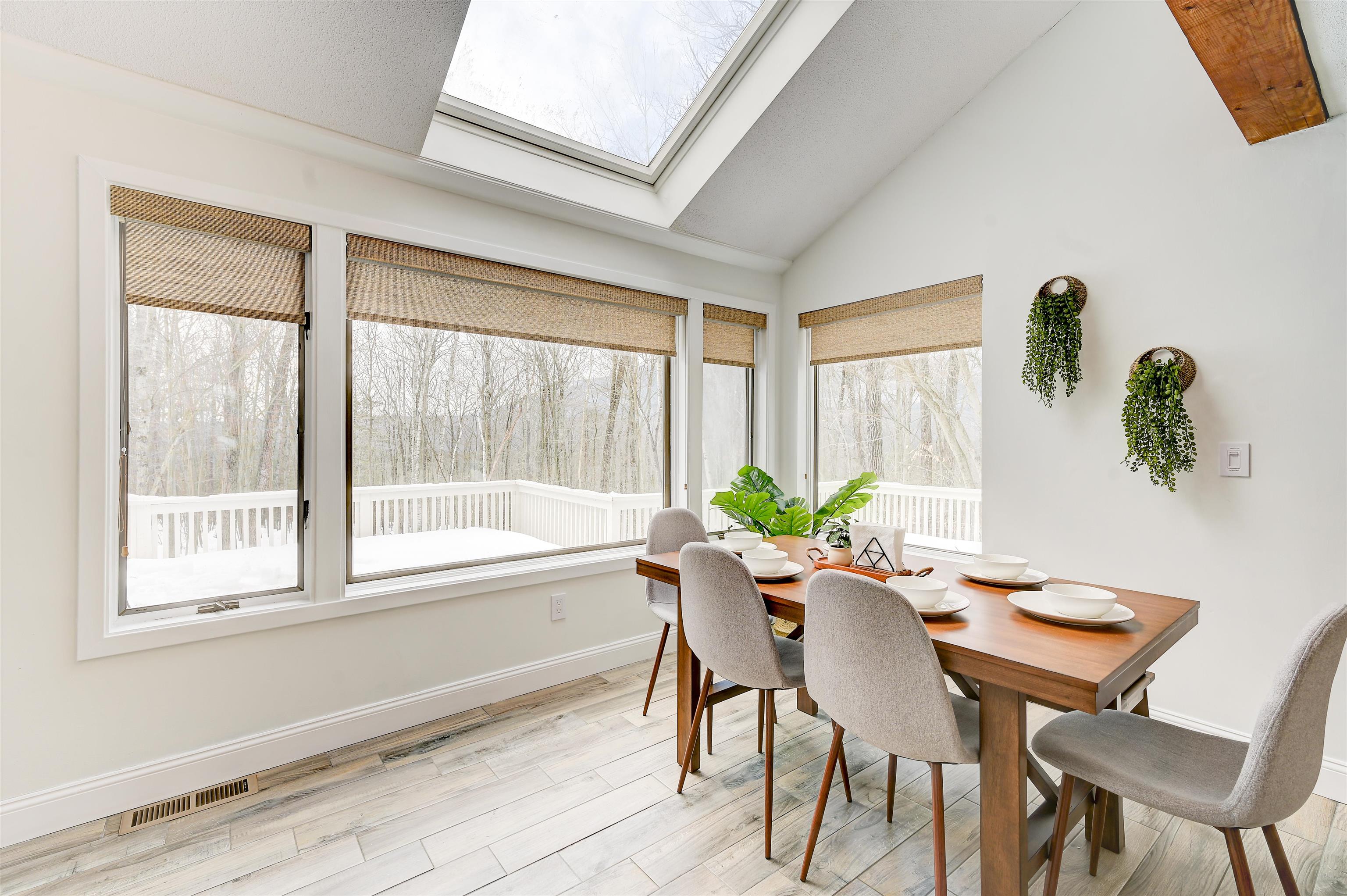Dining room with a skylight, wood table, and windows overlooking snowy woods.