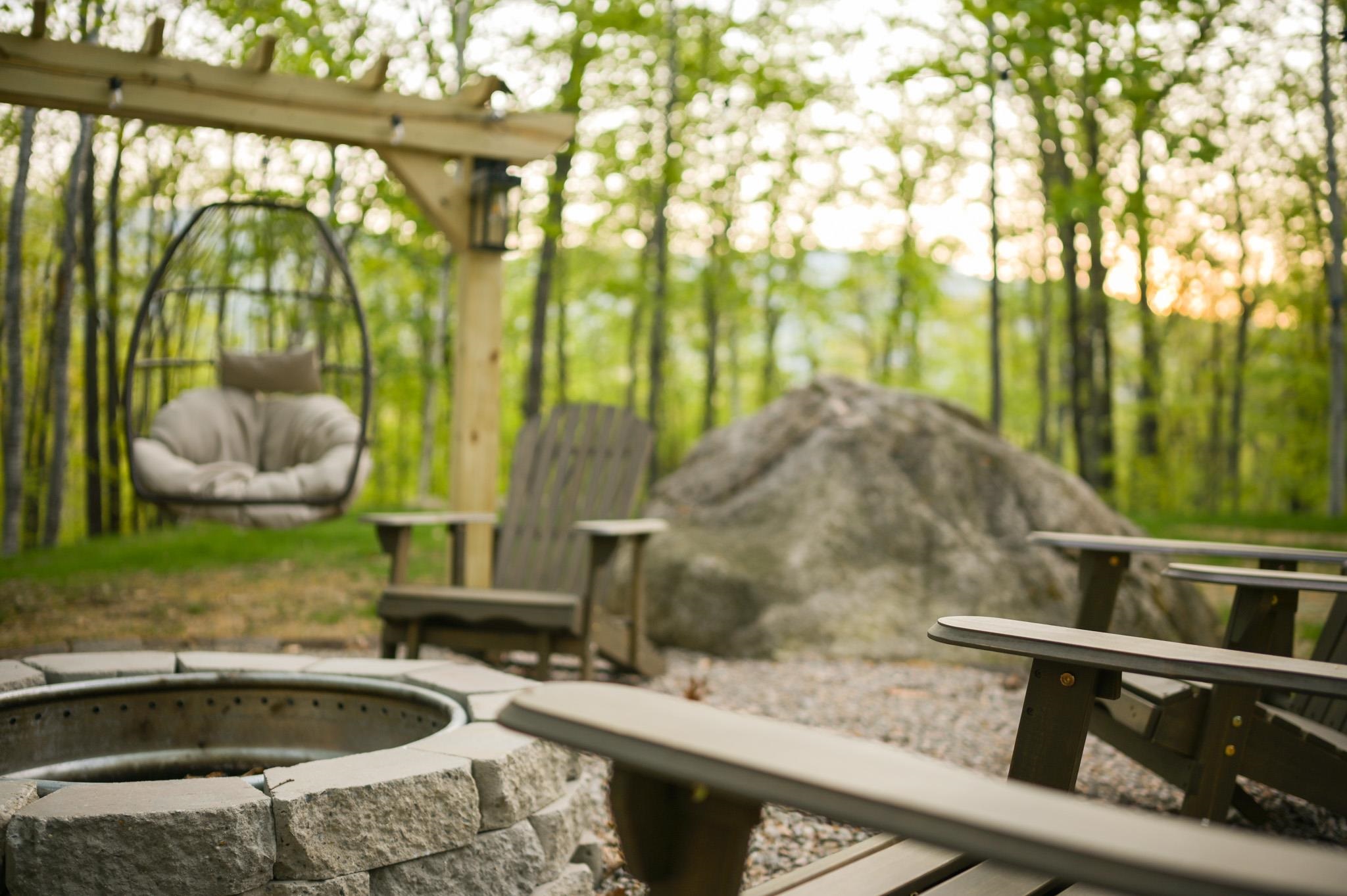 Wooded patio with a stone fire pit, Adirondack chairs, and a hanging egg chair.