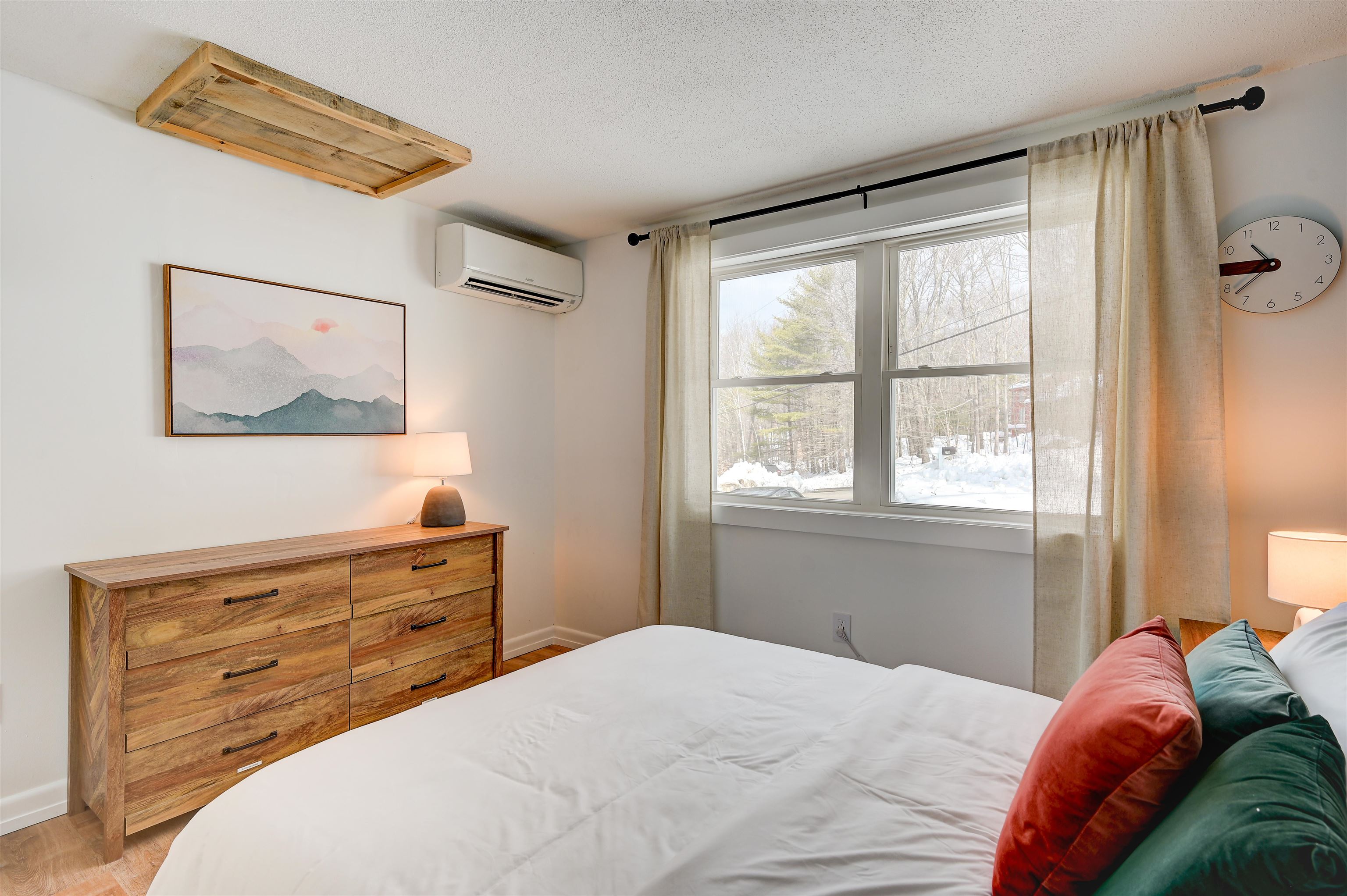 Furnished bedroom with a wood dresser and large windows overlooking snowy woods.