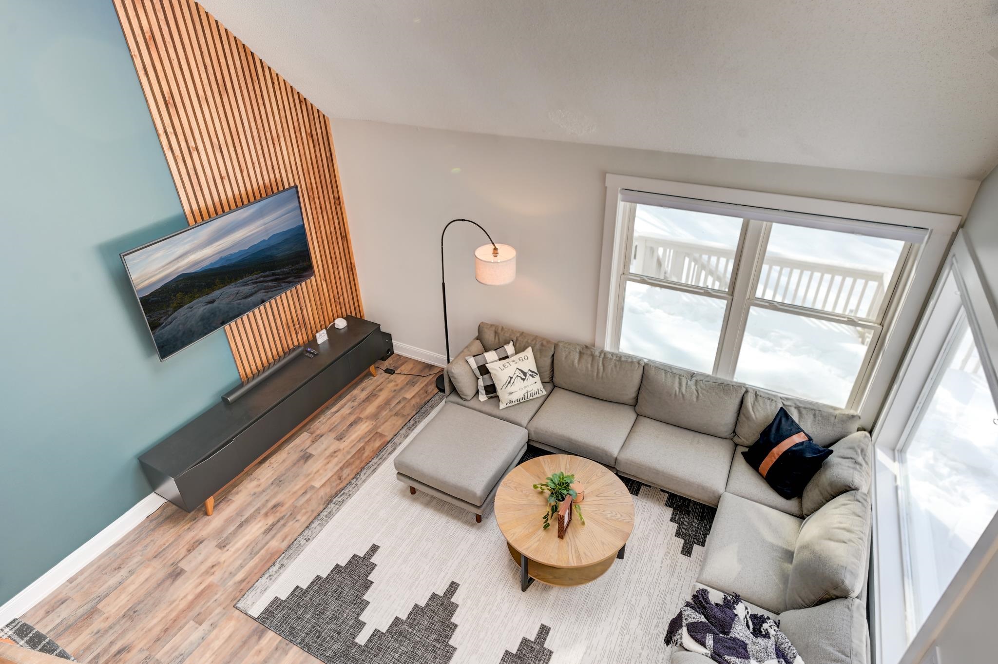 Living room with a gray sectional, round wood coffee table, and windows overlooking a snowy deck.