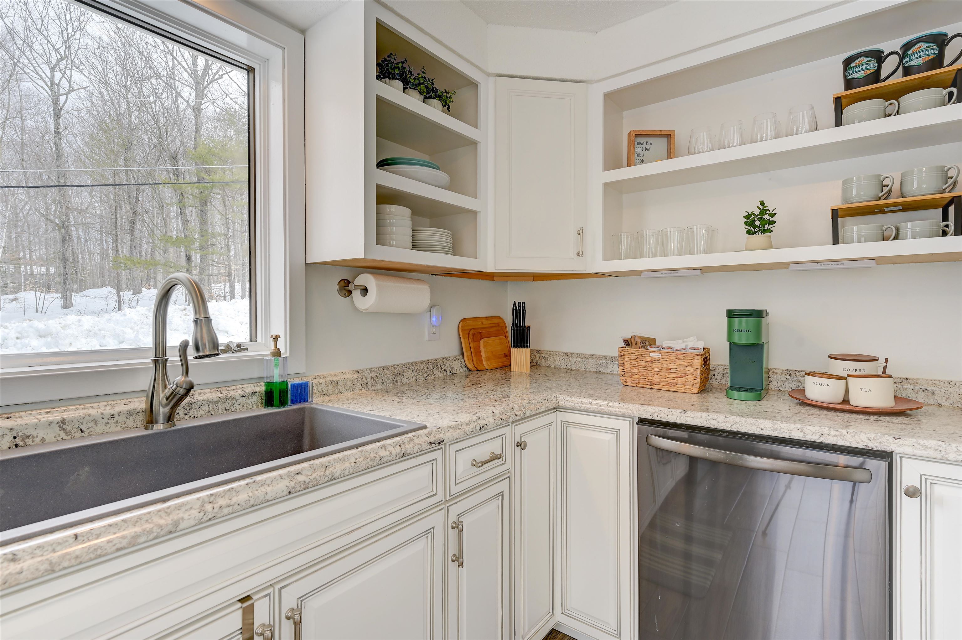 Kitchen with white cabinetry and granite counters, looking out onto a snowy wooded yard.