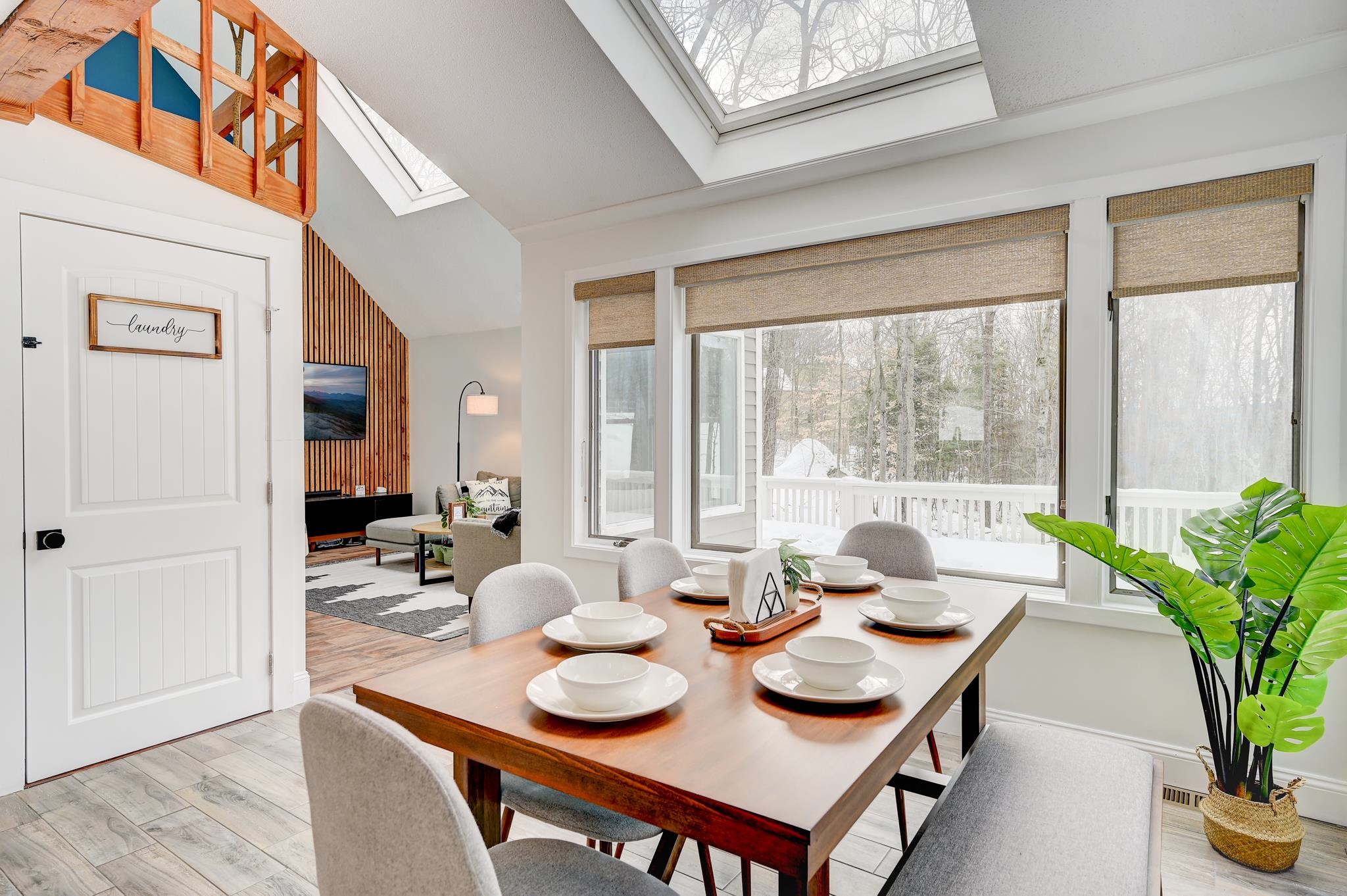 Dining area with a set table, large windows overlooking snowy woods, and a skylight.