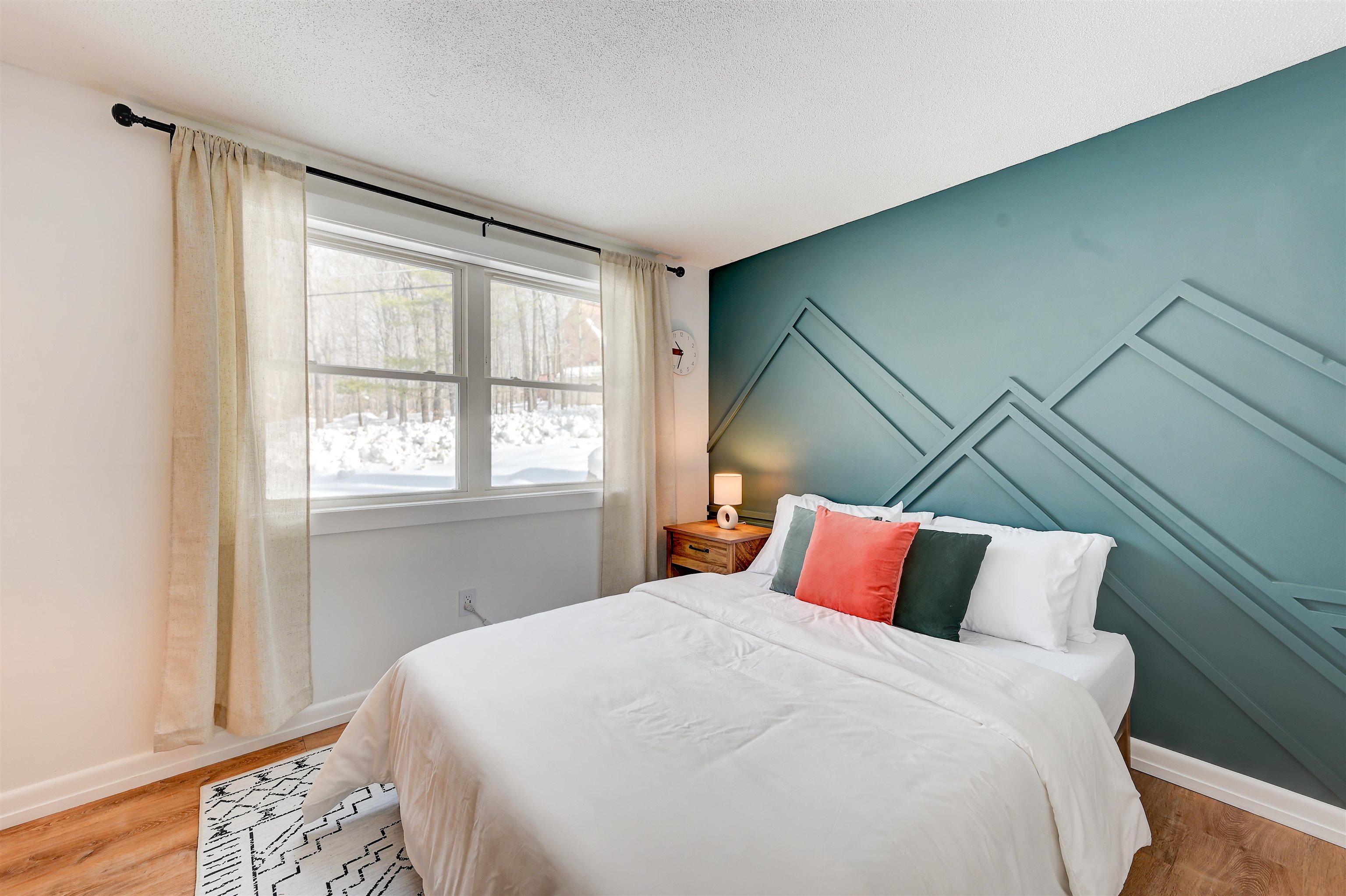 Bedroom with a white bed, teal geometric accent wall, and a window overlooking snow.
