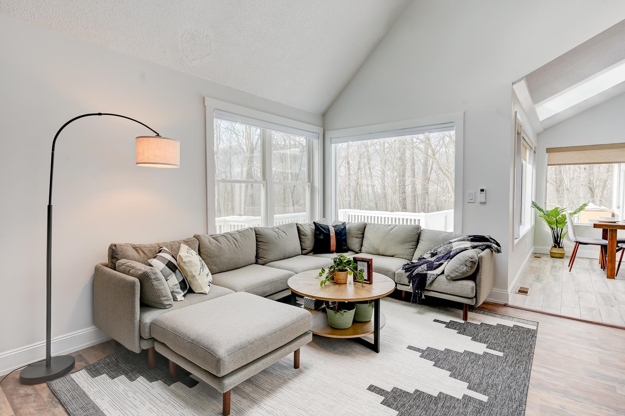 Bright living room with a gray sectional, large windows, and views of trees and a deck.