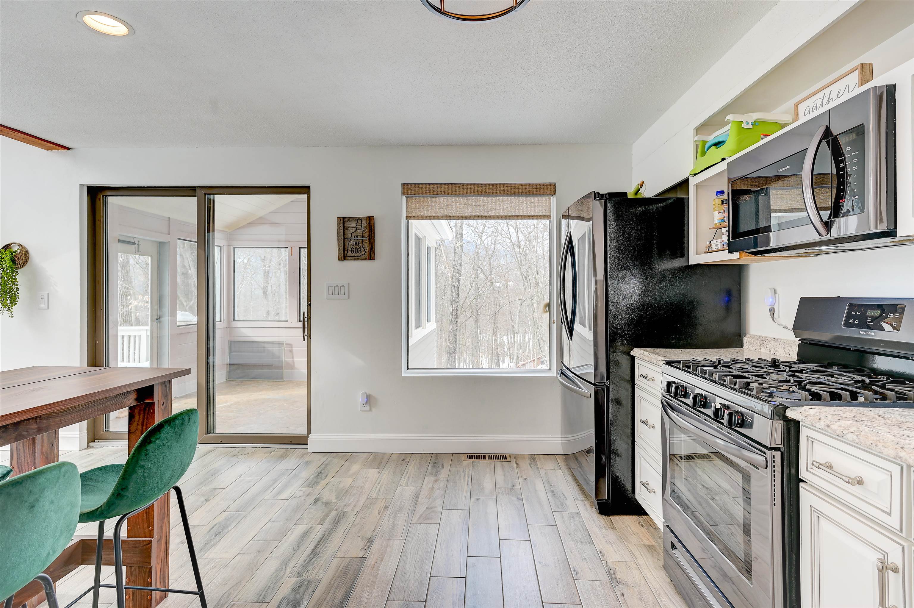 Bright kitchen with stainless steel appliances, white cabinetry, and a sliding door to a sunroom.
