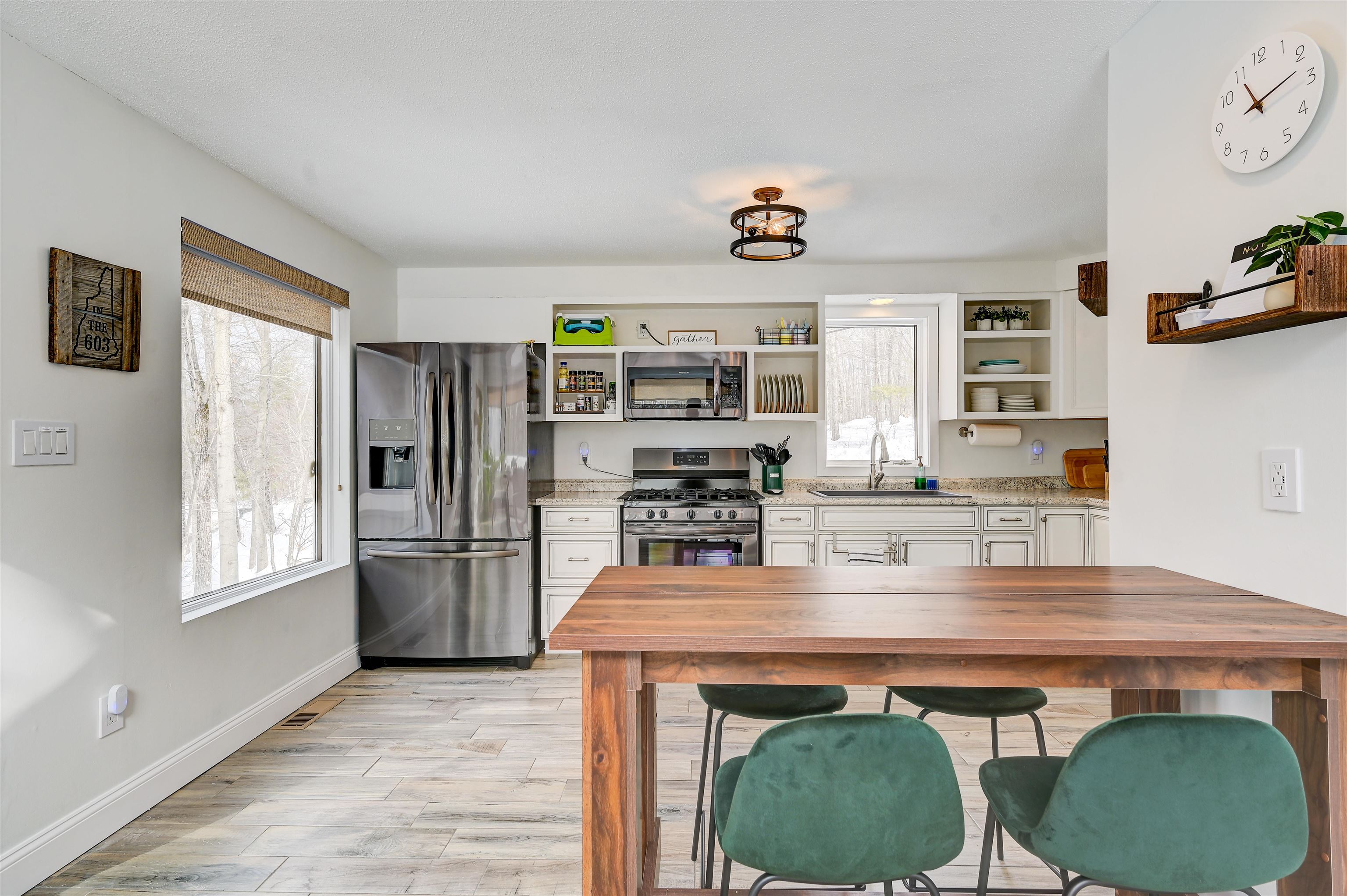 Kitchen with white cabinets, stainless appliances, and a wooden dining table overlooking snowy woods.