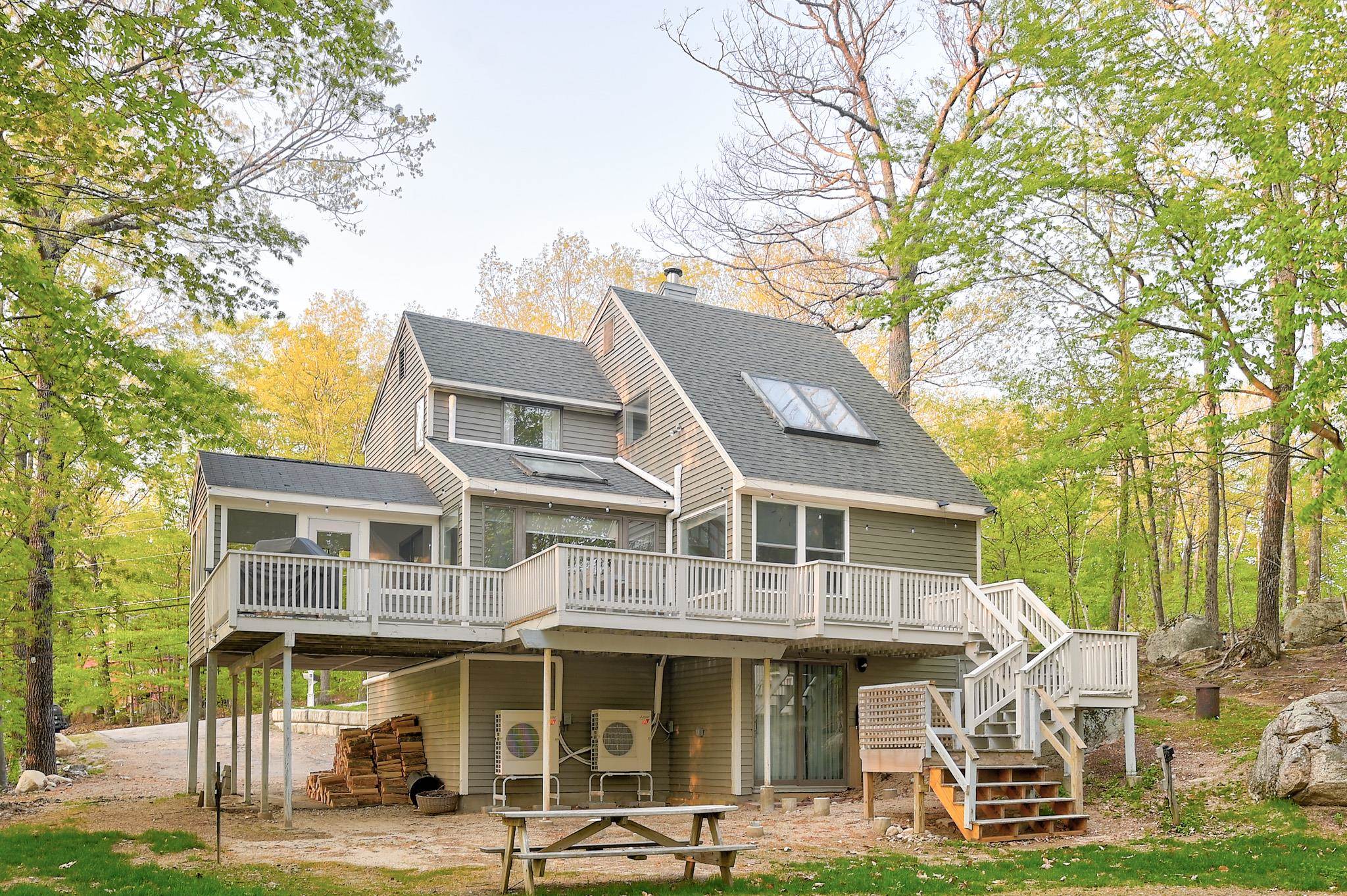 Home’s rear exterior with a large elevated deck and stairs among autumn trees.
