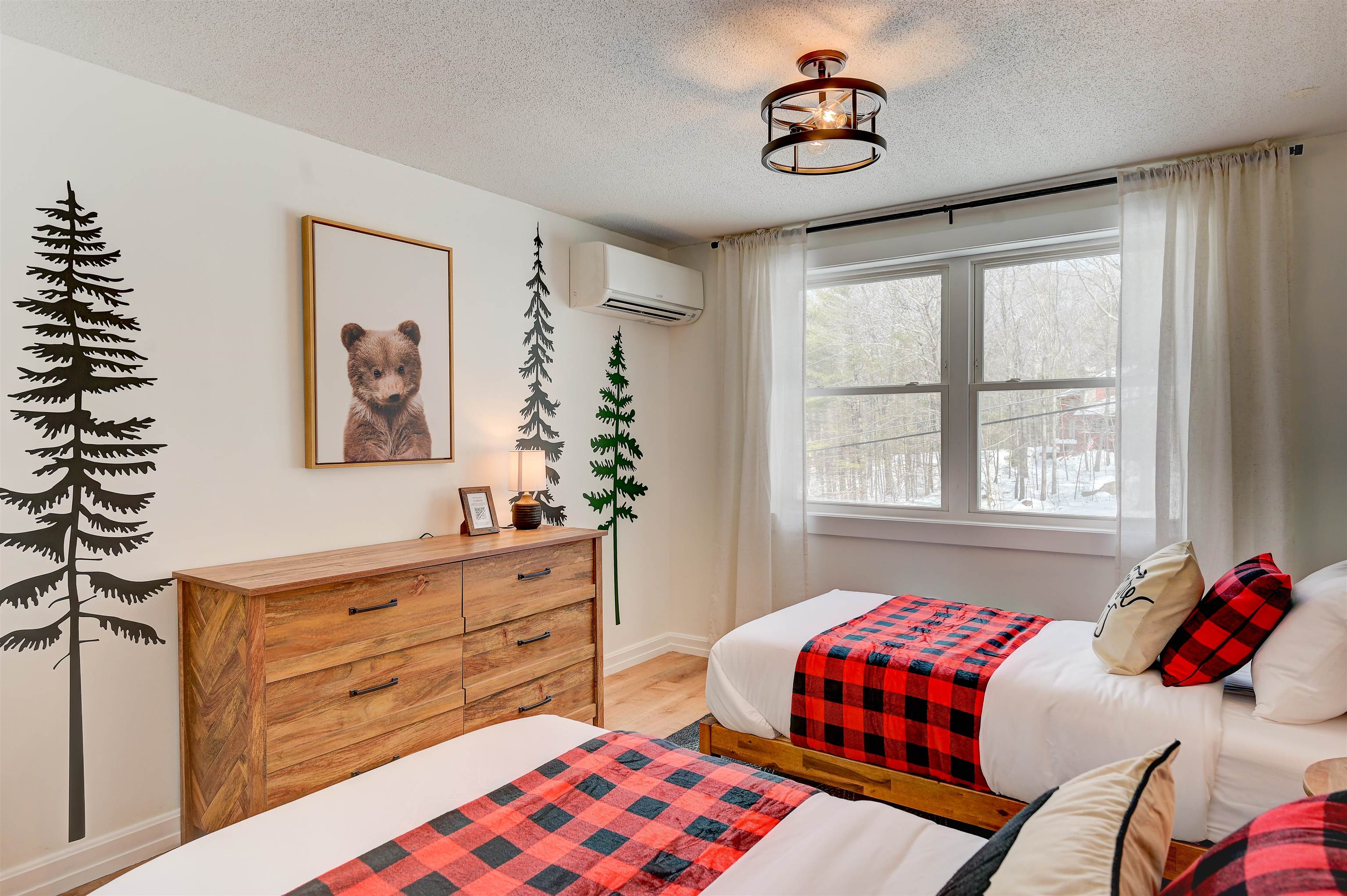 Bedroom with two buffalo-check beds, a rustic wood dresser, and a window overlooking snowy trees.
