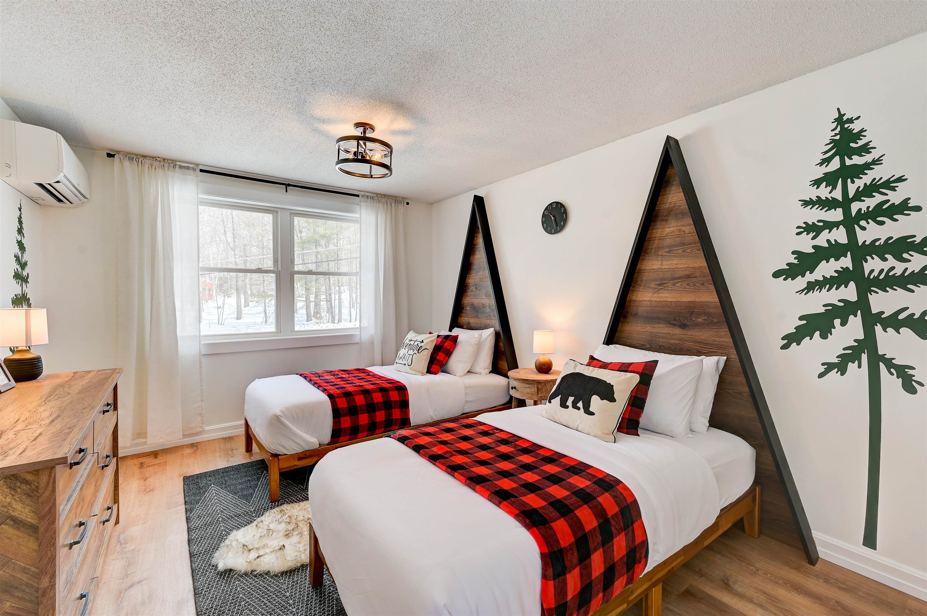 Bedroom with two beds, plaid throws, triangular wood headboards, and a snowy woodland view.