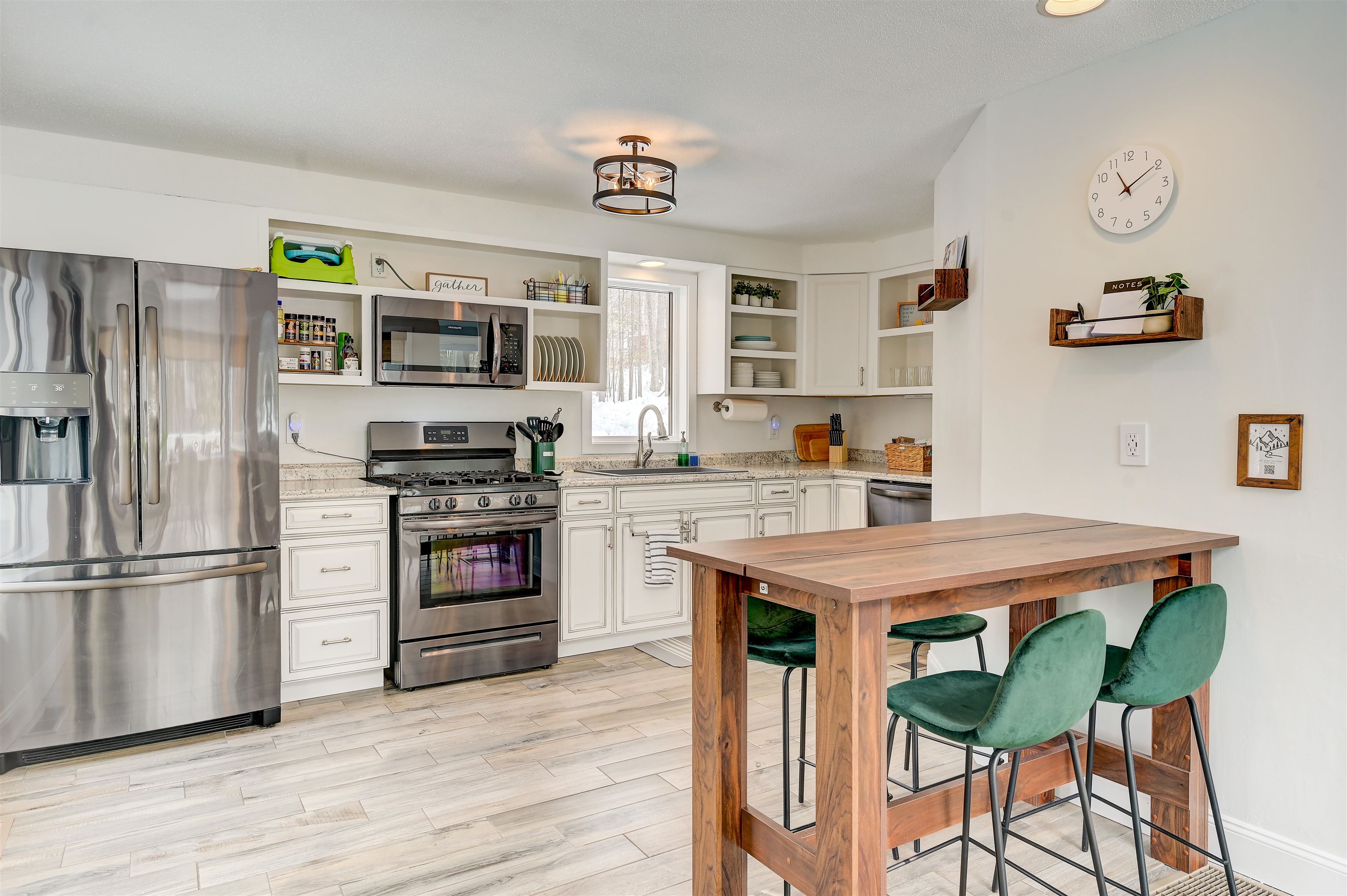 Bright white kitchen with stainless appliances and a wood island surrounded by green stools.