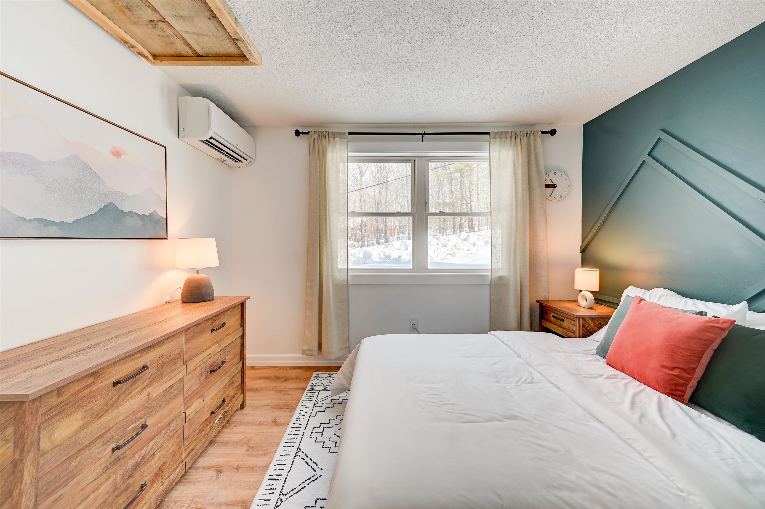 Bedroom with a teal geometric headboard, white bedding, wood furniture, and a snowy view through the window.