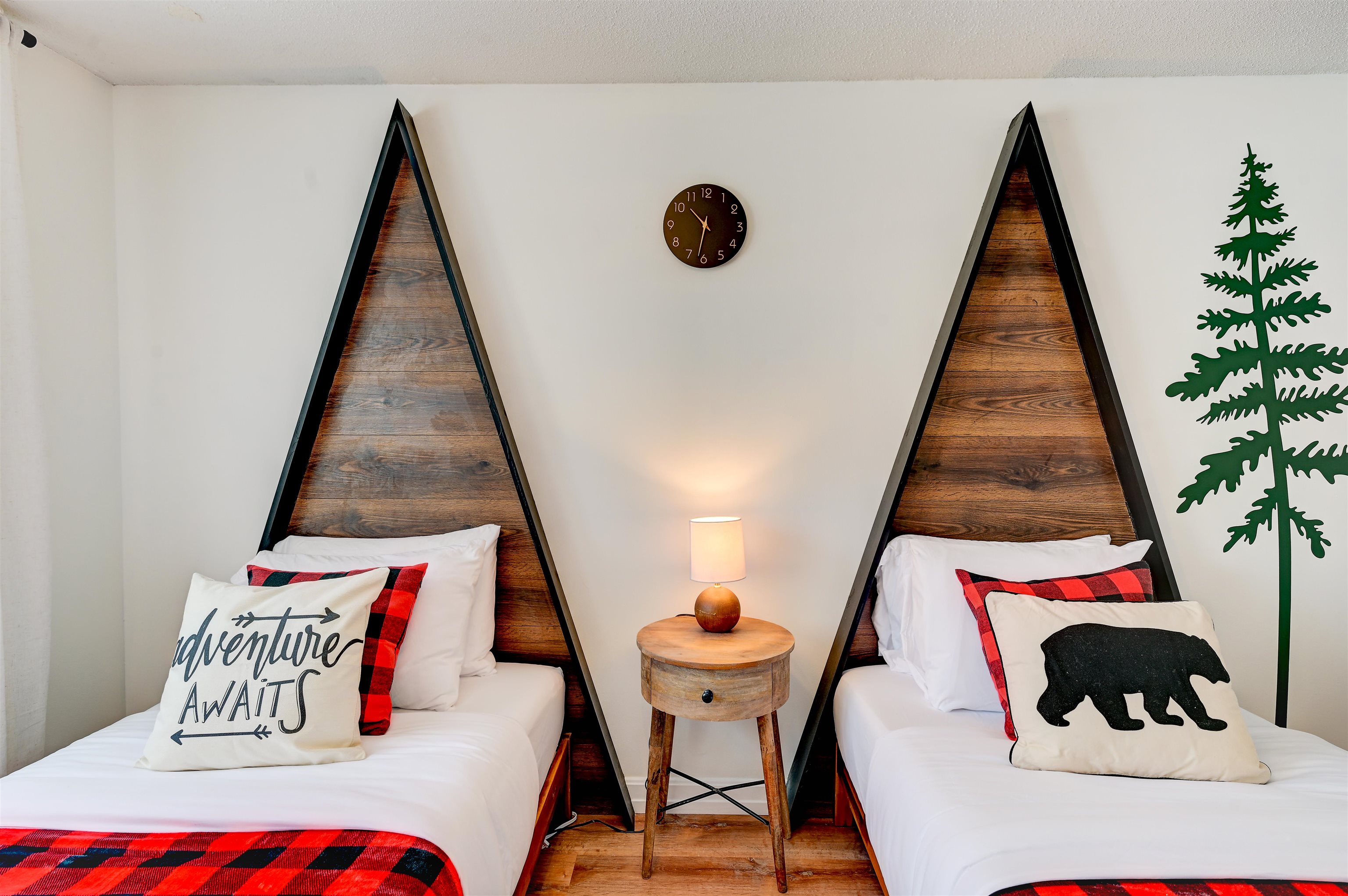 Bedroom with twin beds, triangular wood headboards, plaid bedding, and a shared bedside table.