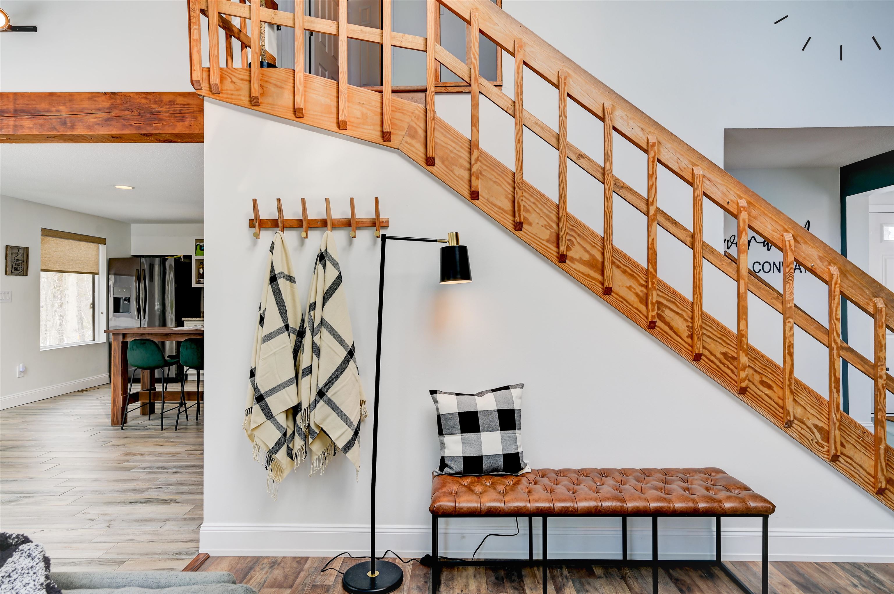 Foyer with a sweeping natural wood staircase, leather bench, and open kitchen and dining area.