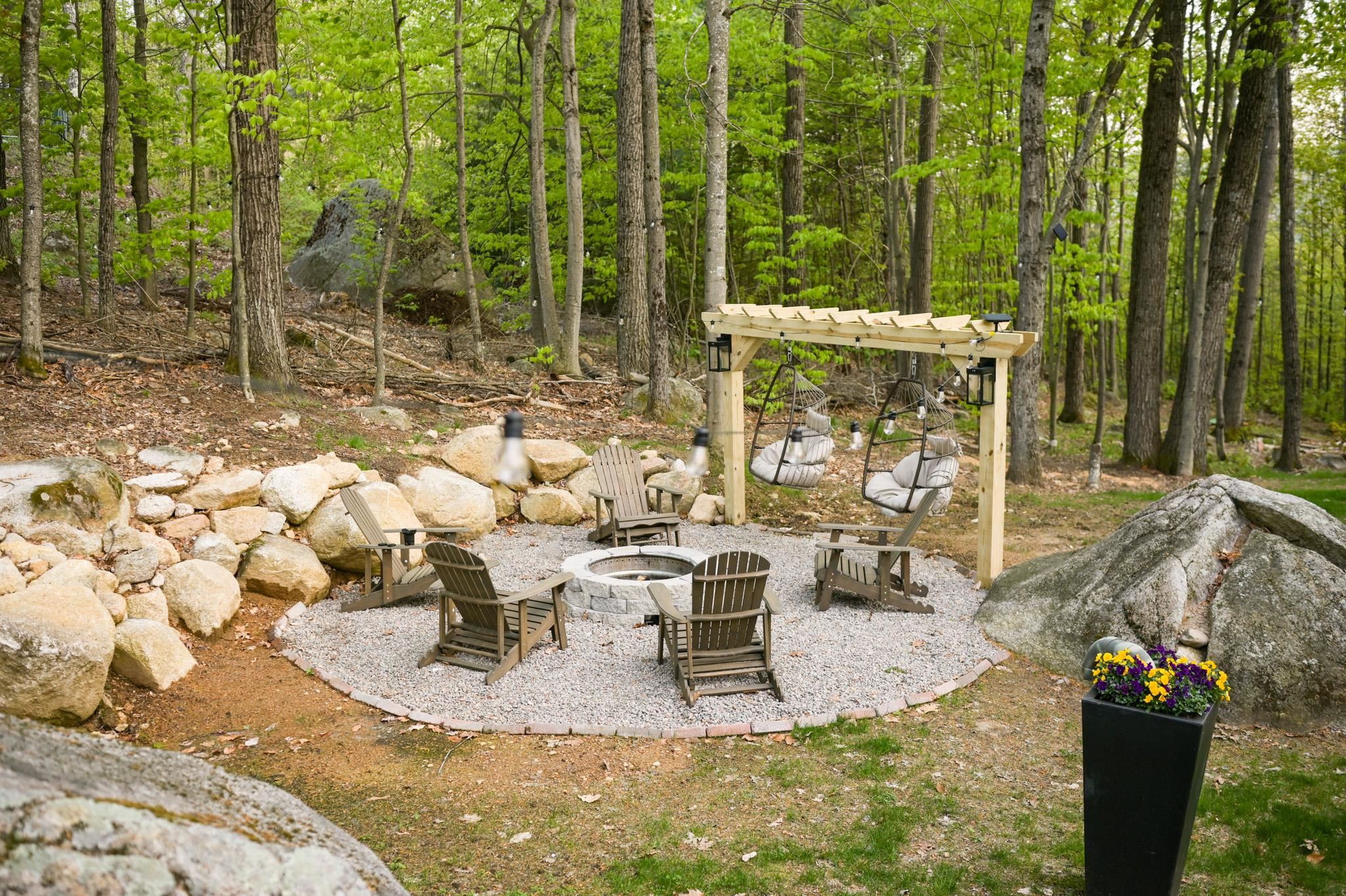 Woodland patio with a stone fire pit, Adirondack chairs, and a pergola with hanging chairs.