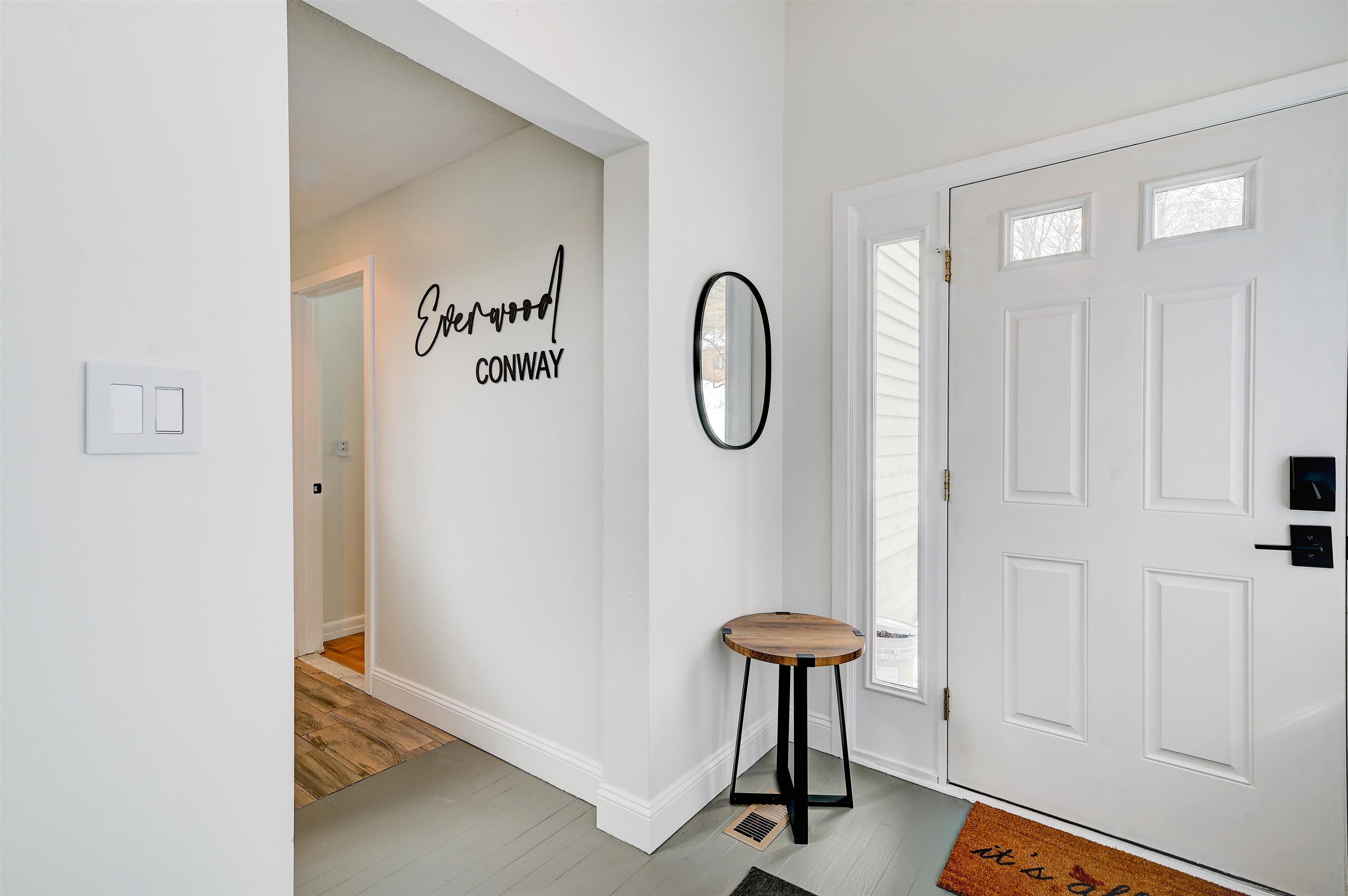 Entry foyer with a white paneled front door, oval mirror, and small round wooden table.
