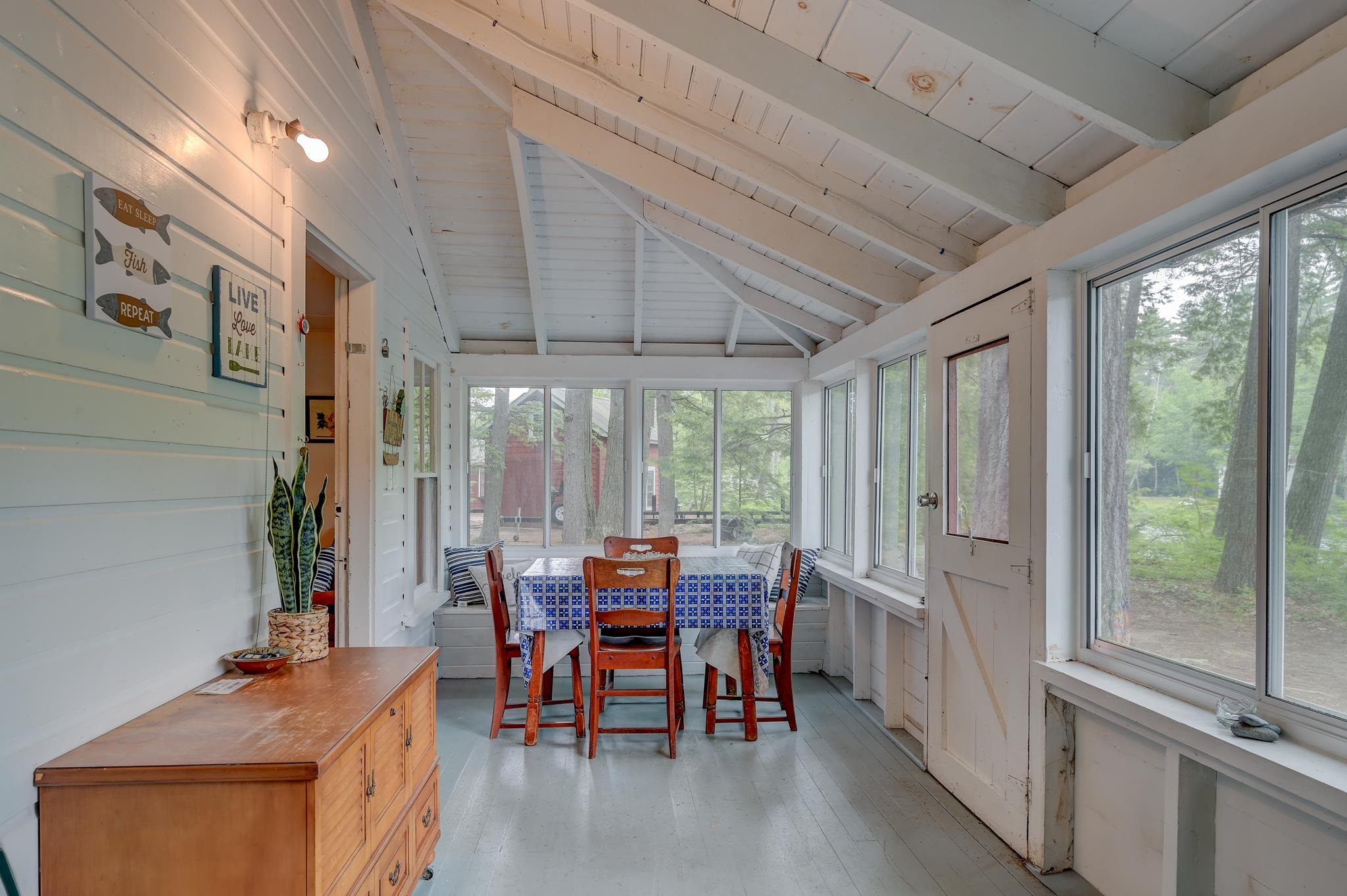 Sunroom dining area with a vaulted beam ceiling, wooden table, and wide windows overlooking trees.