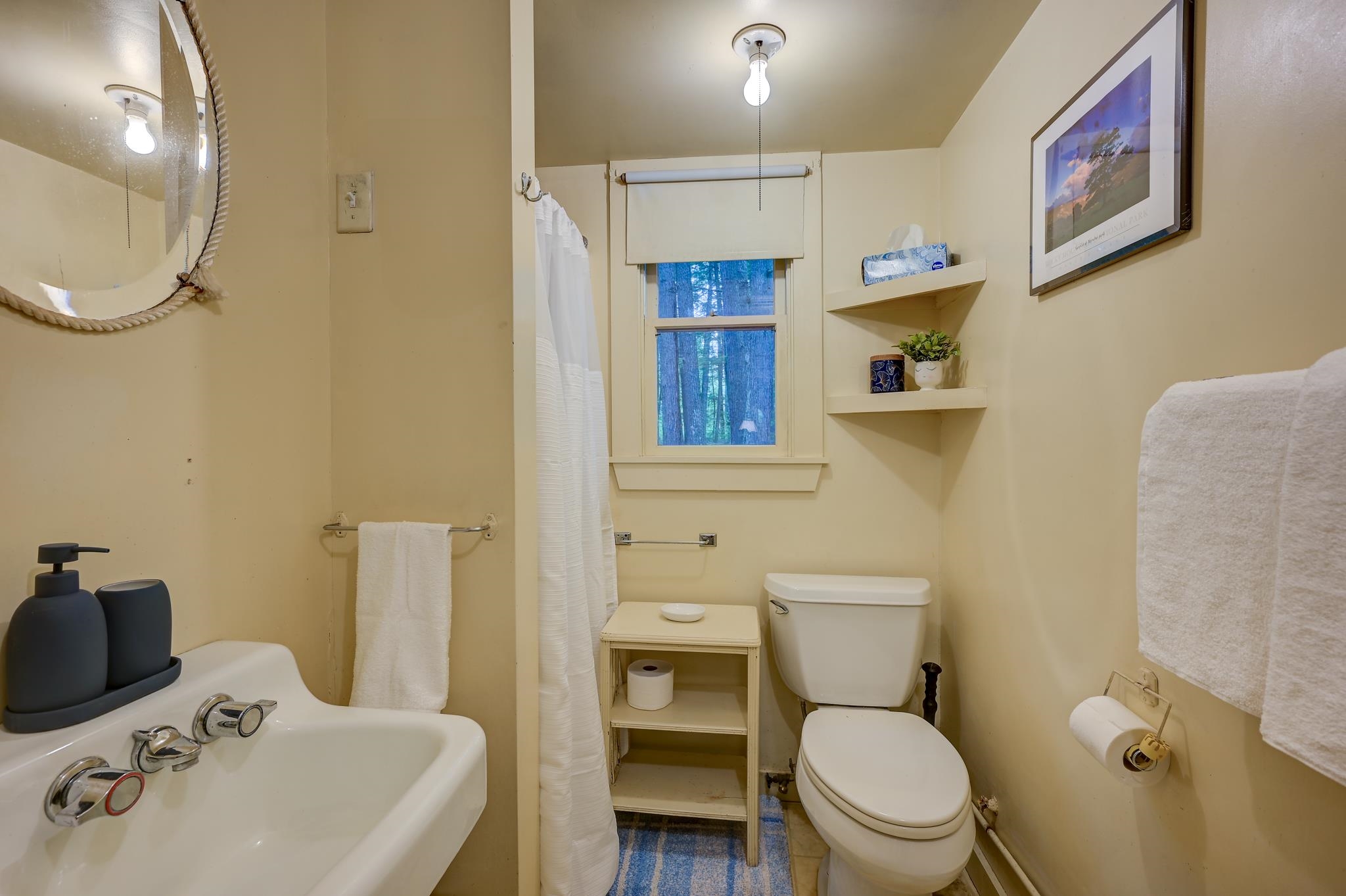 Bathroom with a white tub, toilet, window overlooking trees, and blue striped rug.