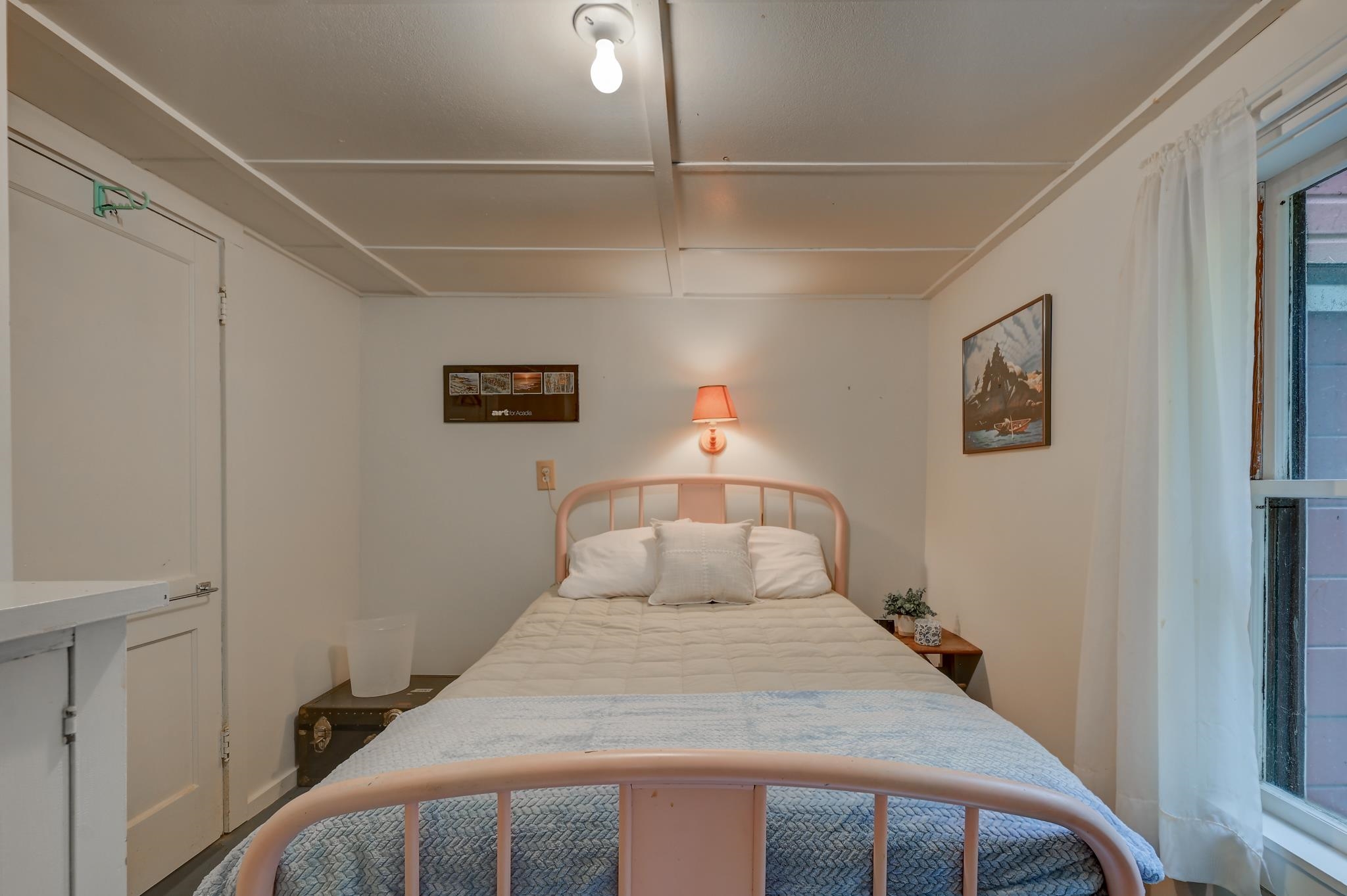 Bedroom with a pink metal bed, white bedding, and a large curtained window.