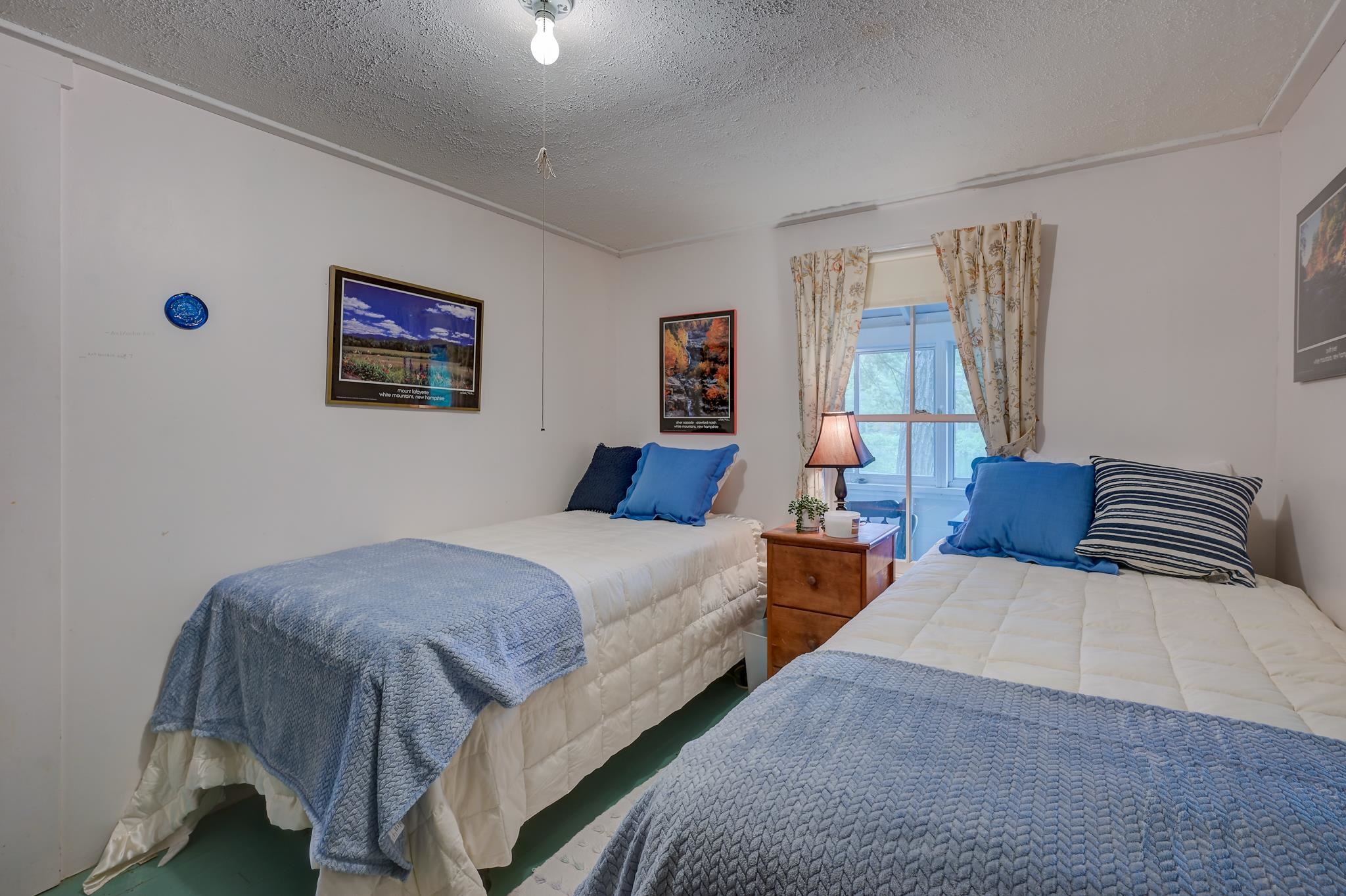 Bedroom with two single beds, blue throws, and a curtained window between them.