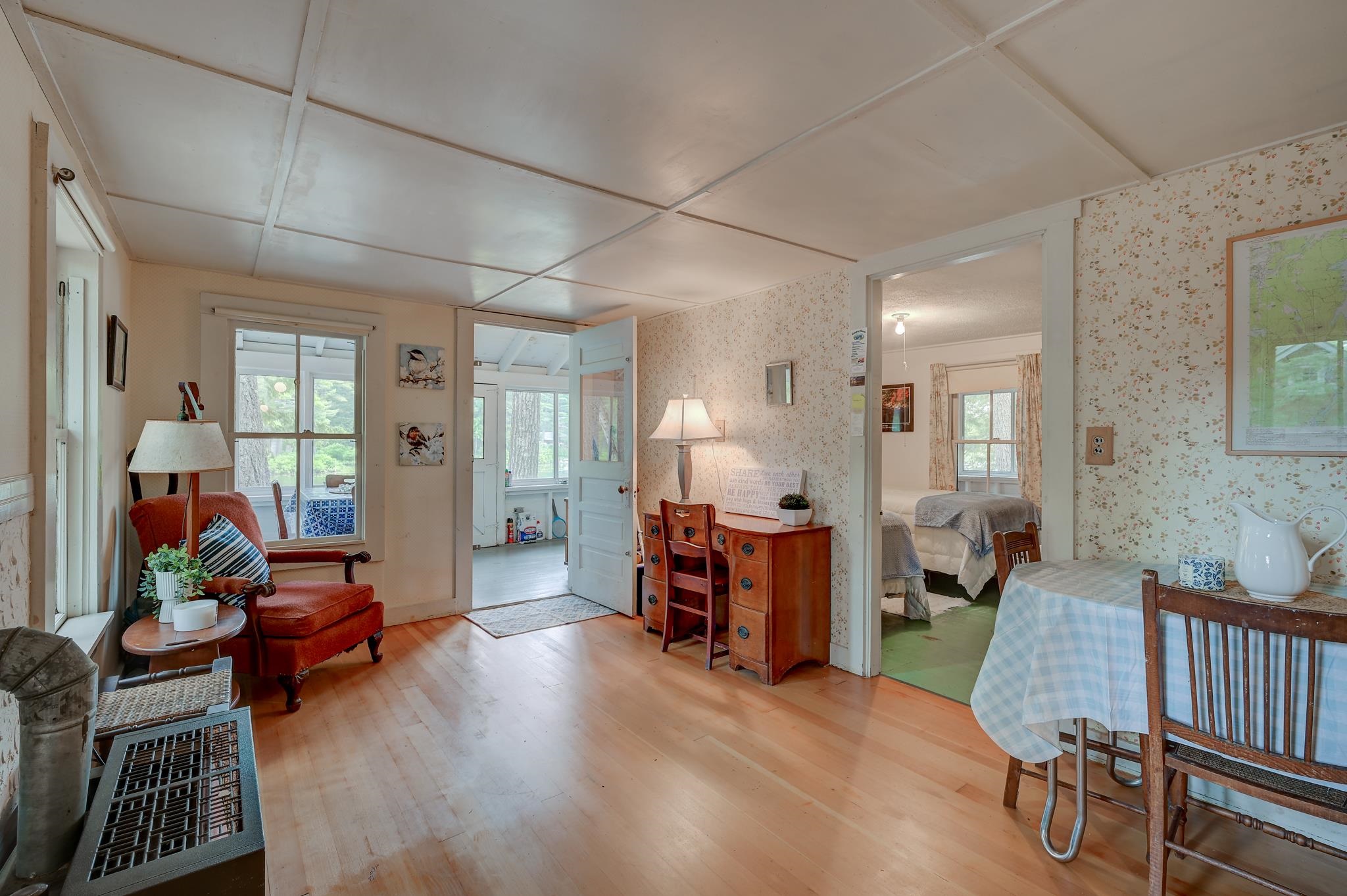 Living and dining area with a red leather armchair, floral wallpaper, and bedroom doorway.