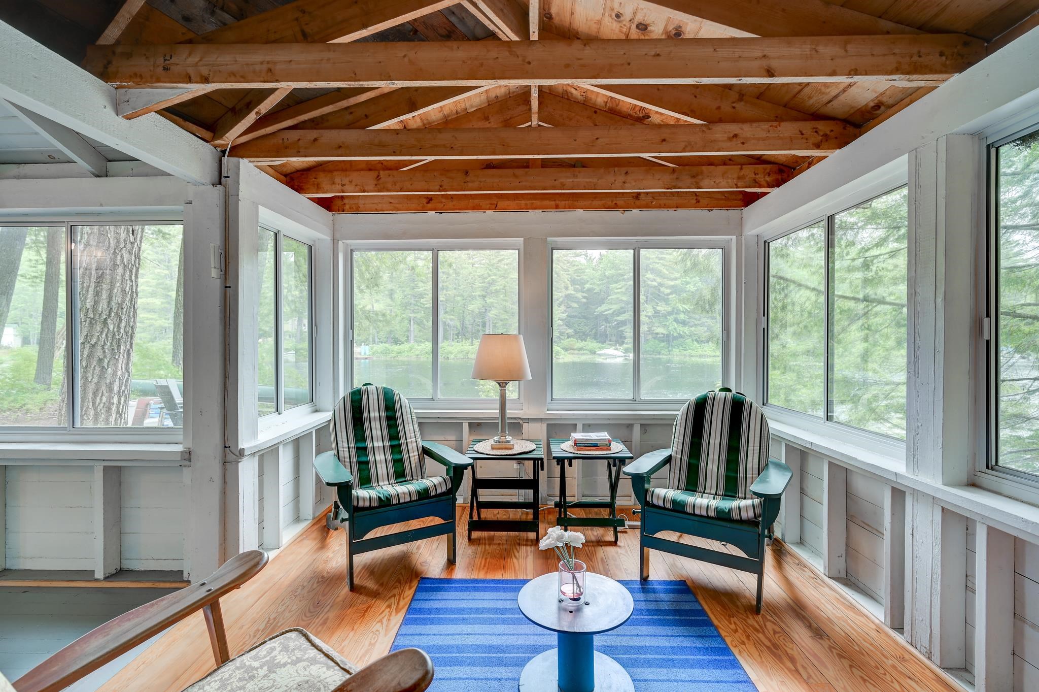 Sunroom with lake views, two striped armchairs, and an exposed timber ceiling.