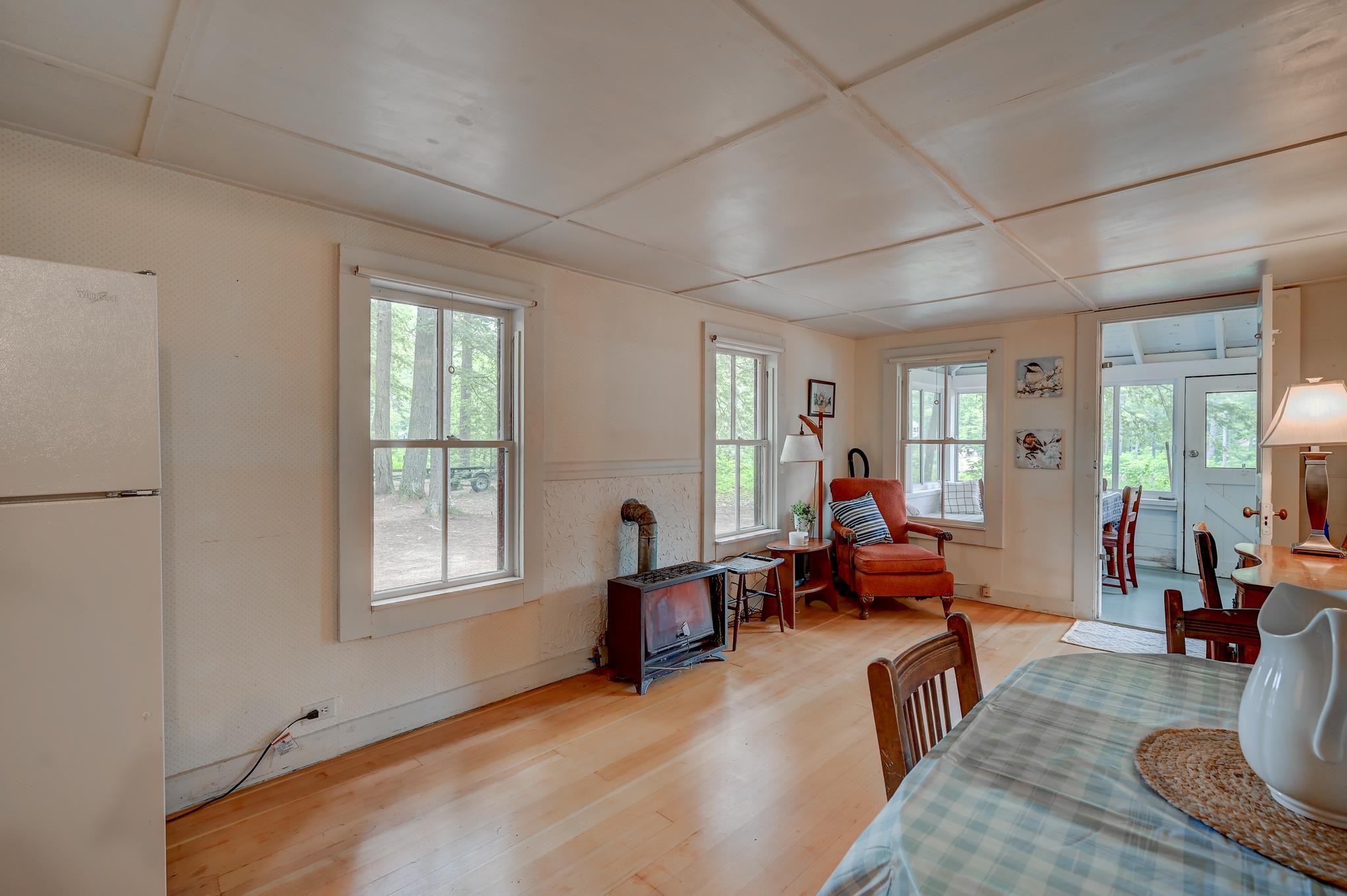 Living and dining area with a wood stove, red armchair, large windows, and dining table.