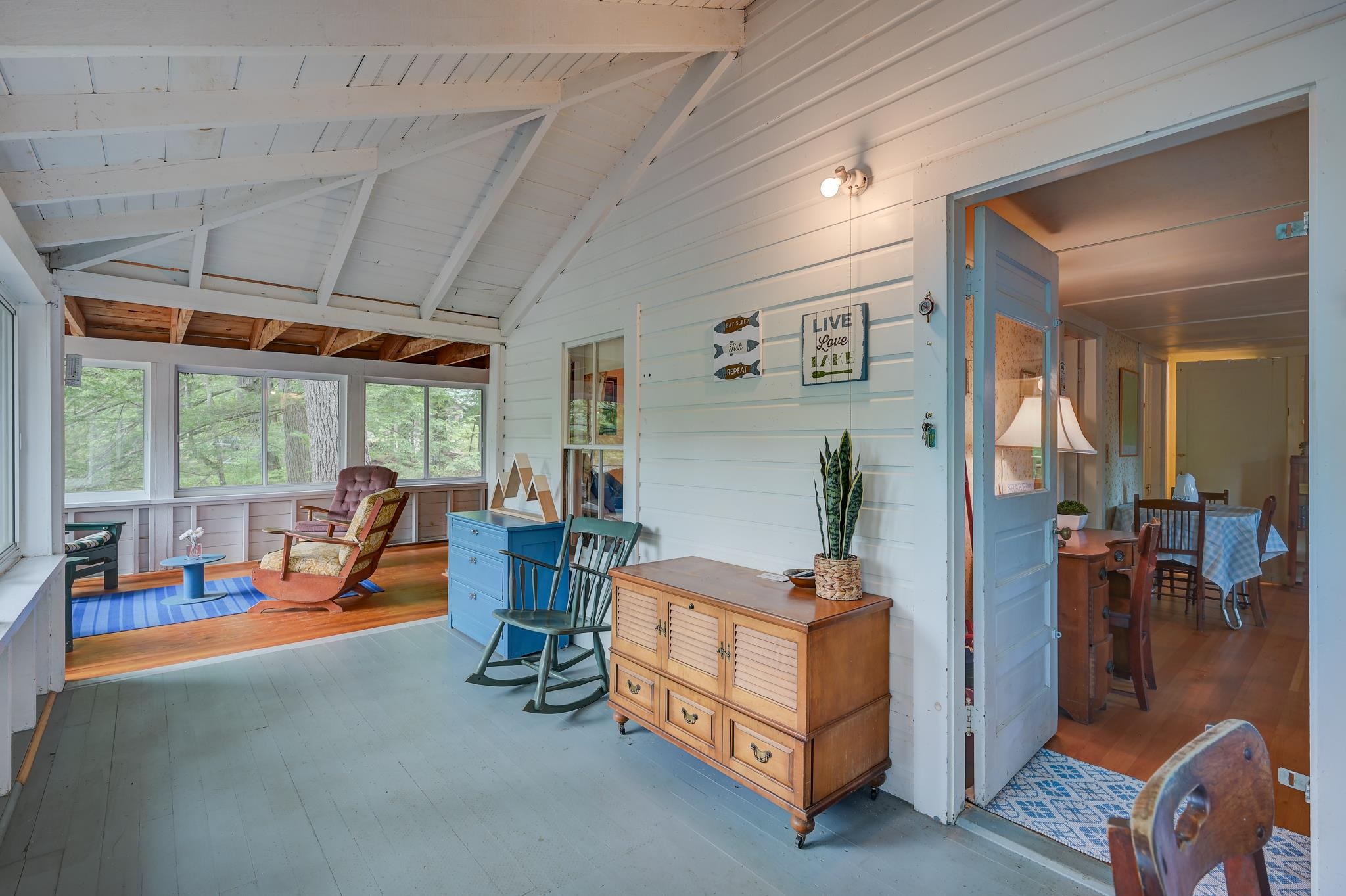 Enclosed sunroom with a vaulted ceiling, tree views, rocking chairs, and an open door to the dining area.