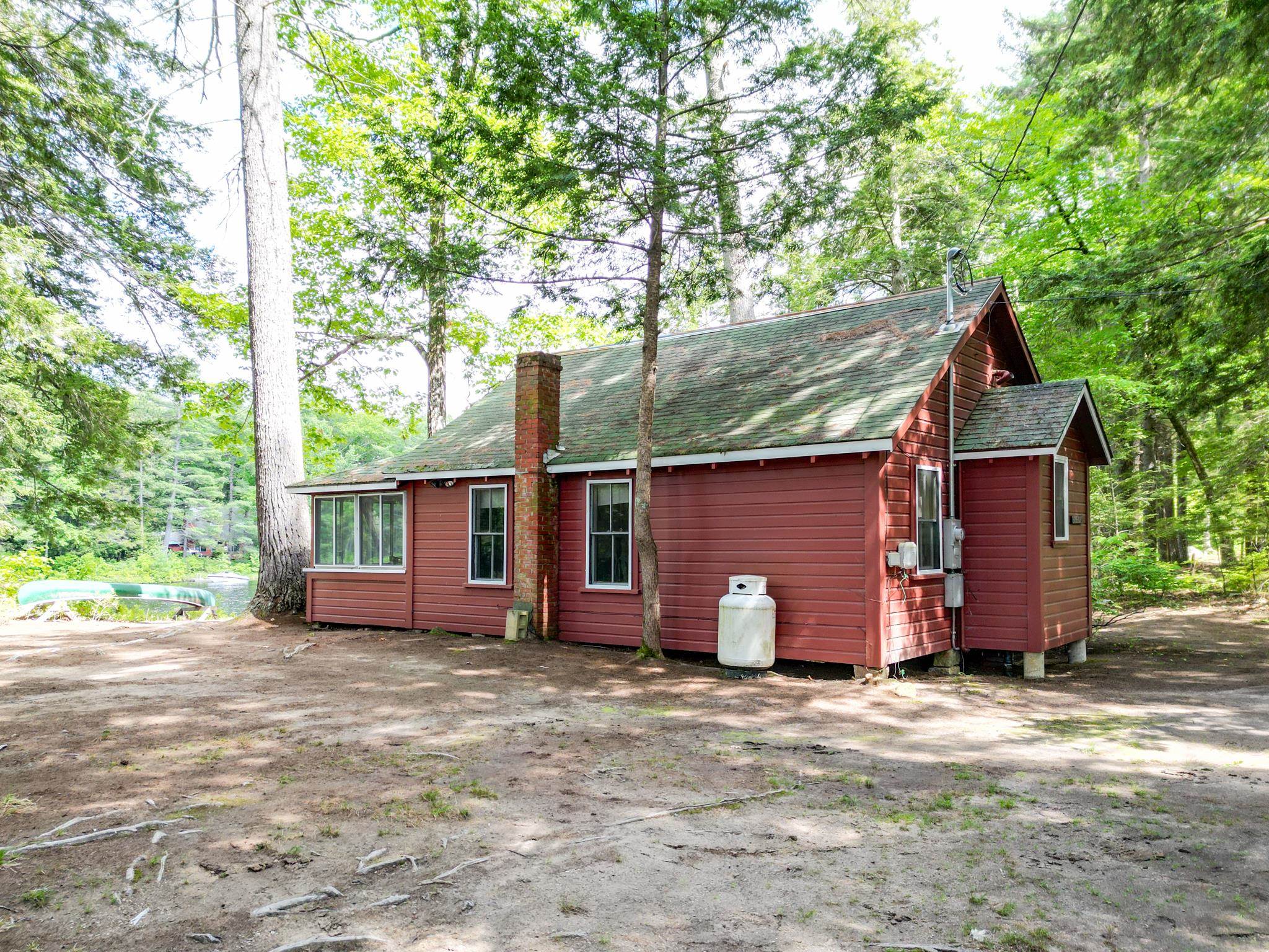 Red-sided house with a green roof and brick chimney among trees, with a canoe beside it.