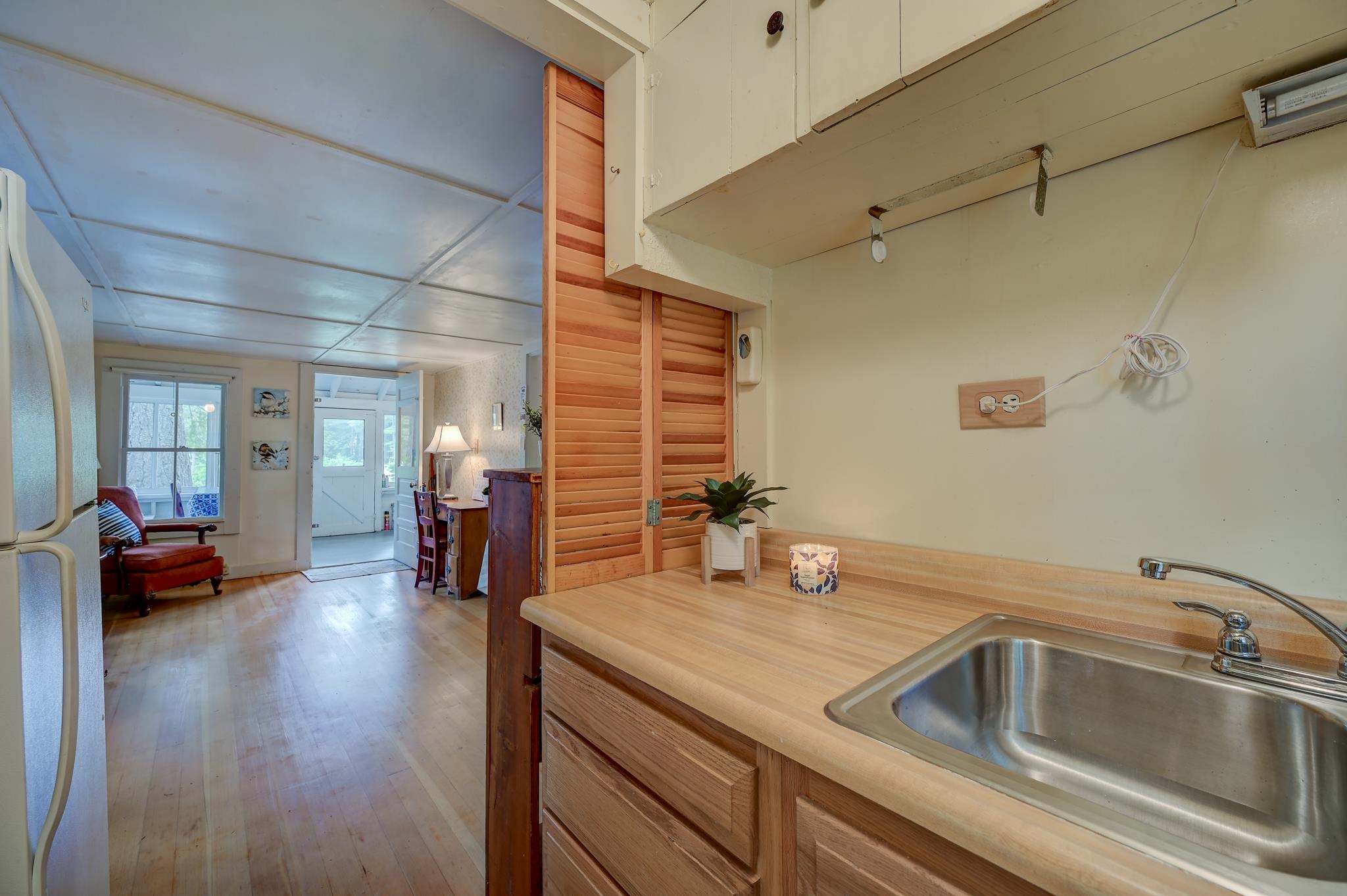 Kitchen with a stainless-steel sink, wood countertops, and louvered doors opening to a sitting area.