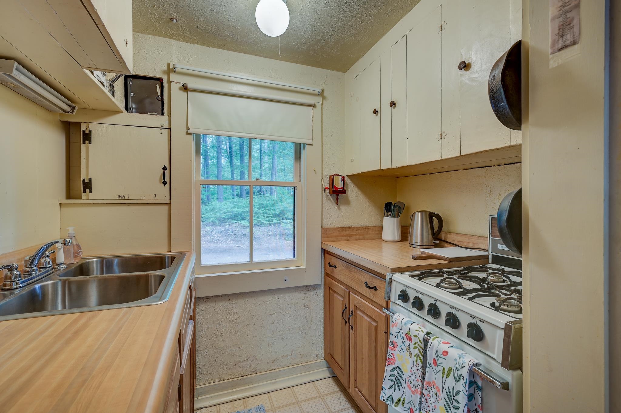 Kitchen with wood counters, a double sink, gas range, and a window overlooking leafy woods.