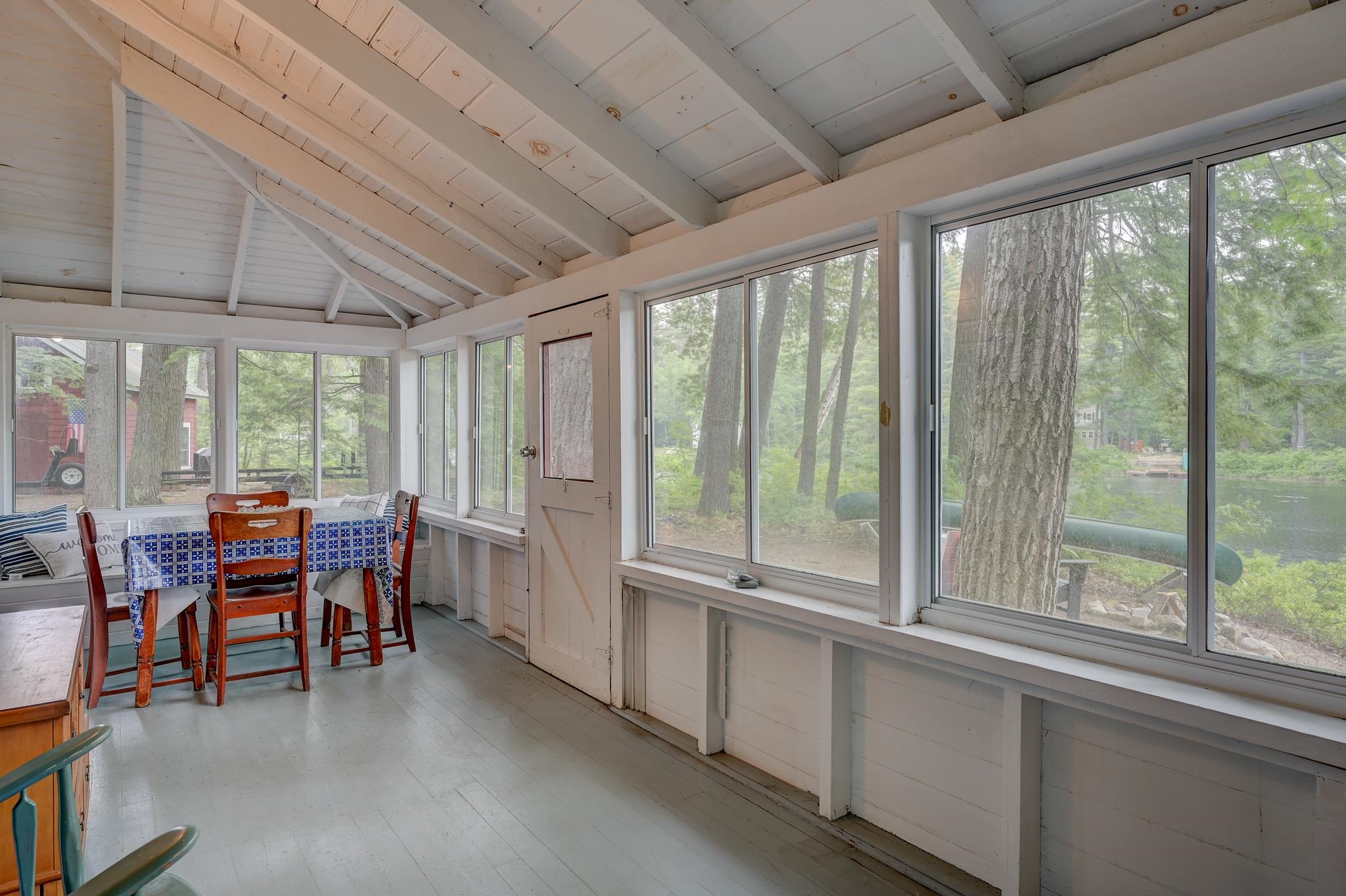 Enclosed sunroom with a vaulted wood ceiling, wraparound windows, and views of trees and water.