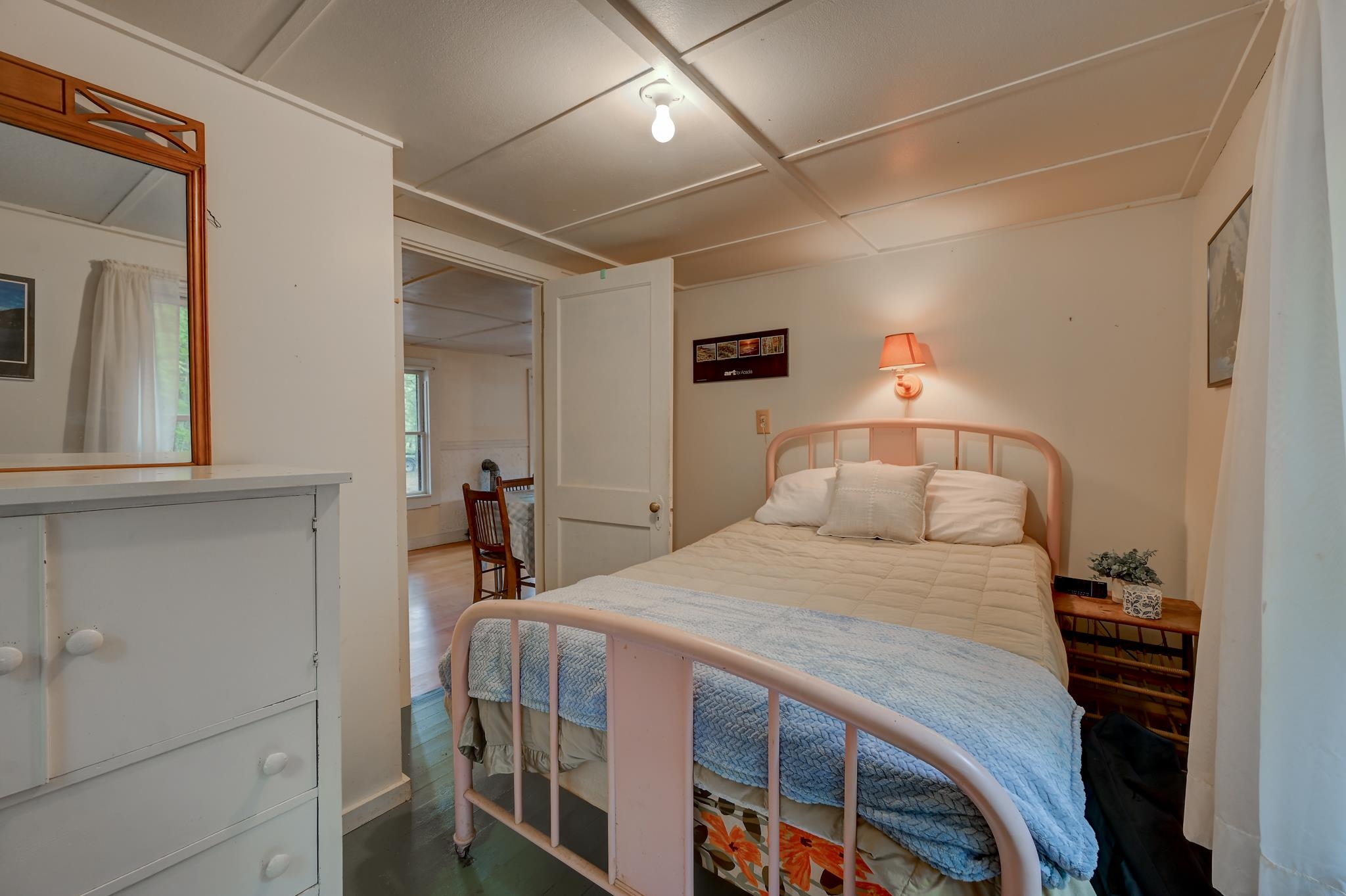 Bedroom with a pink metal bed frame, blue blanket, and white dresser with a large mirror.