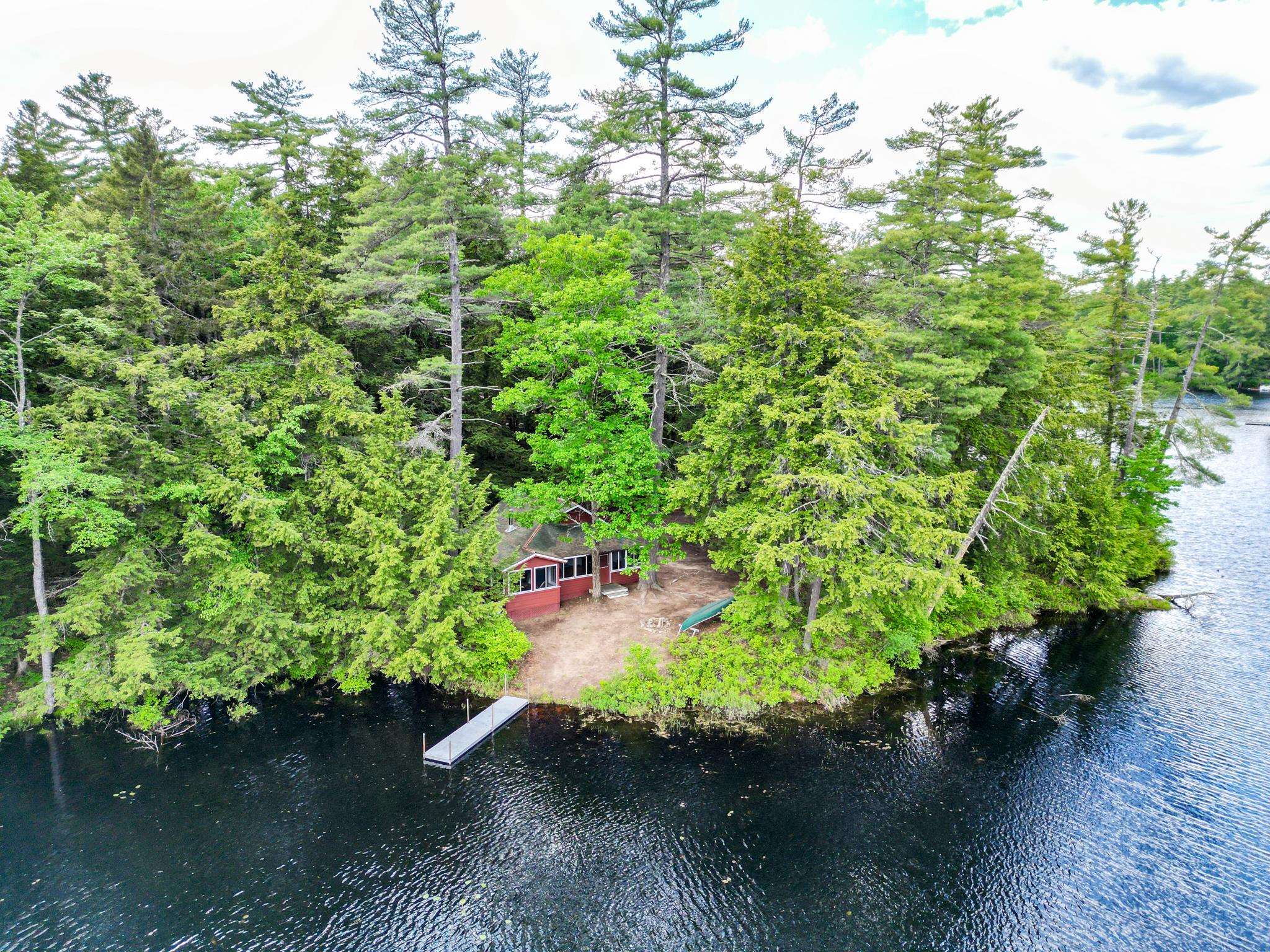Aerial view of a red lakeside home among trees, with a dock on the water.